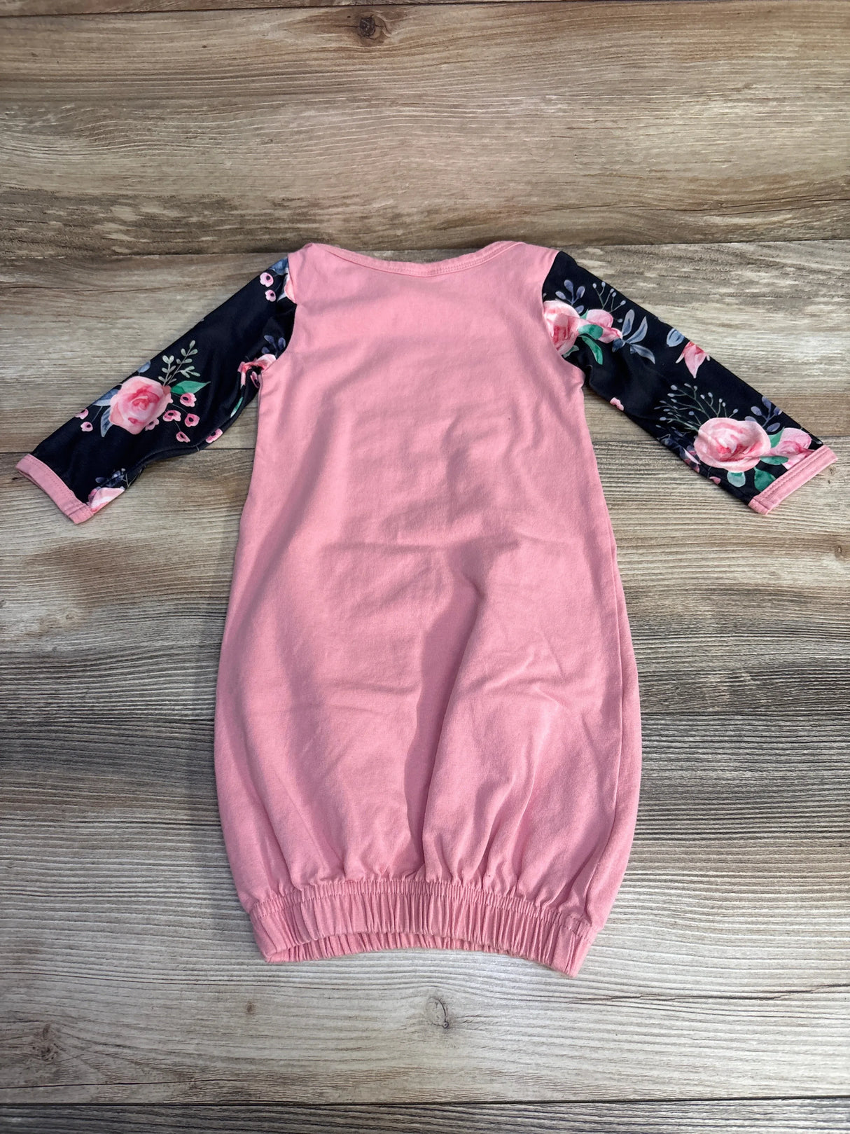 Flat lay of Little Sis baby gown in pink with black floral long sleeves and elastic gathered bottom on wood background