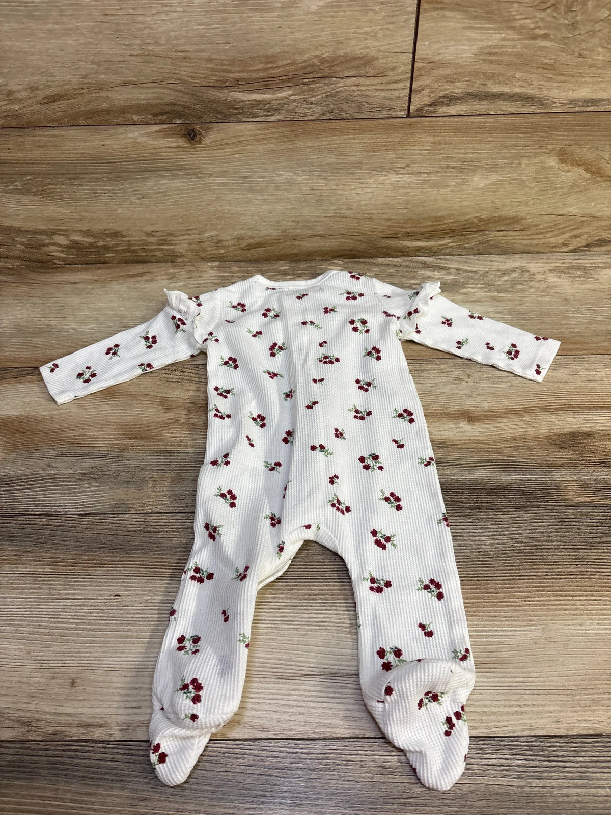 Flat lay of 7 For All Mankind white thermal footed sleeper showing red floral print, ruffle shoulders, and waffle texture on wood background