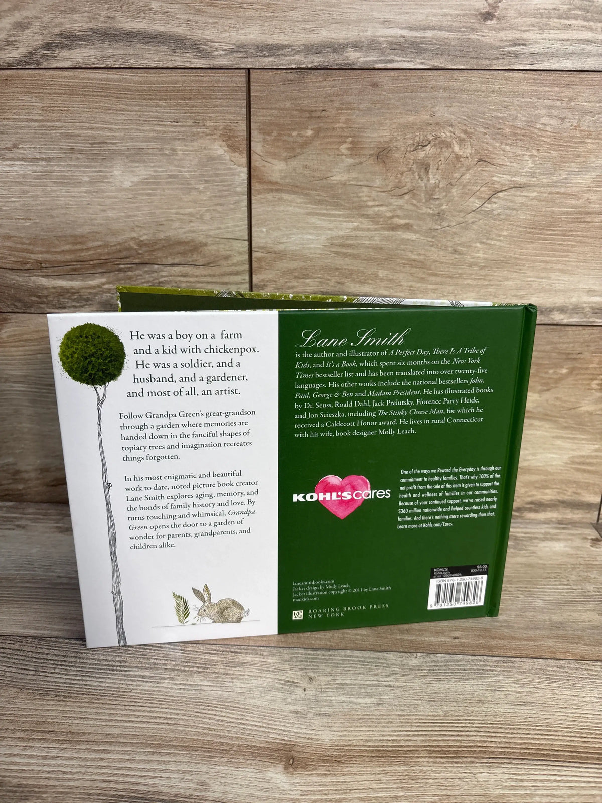 Back view of Grandpa Green Hardcover Book showcasing its green back cover with story text and illustrations on a wood surface