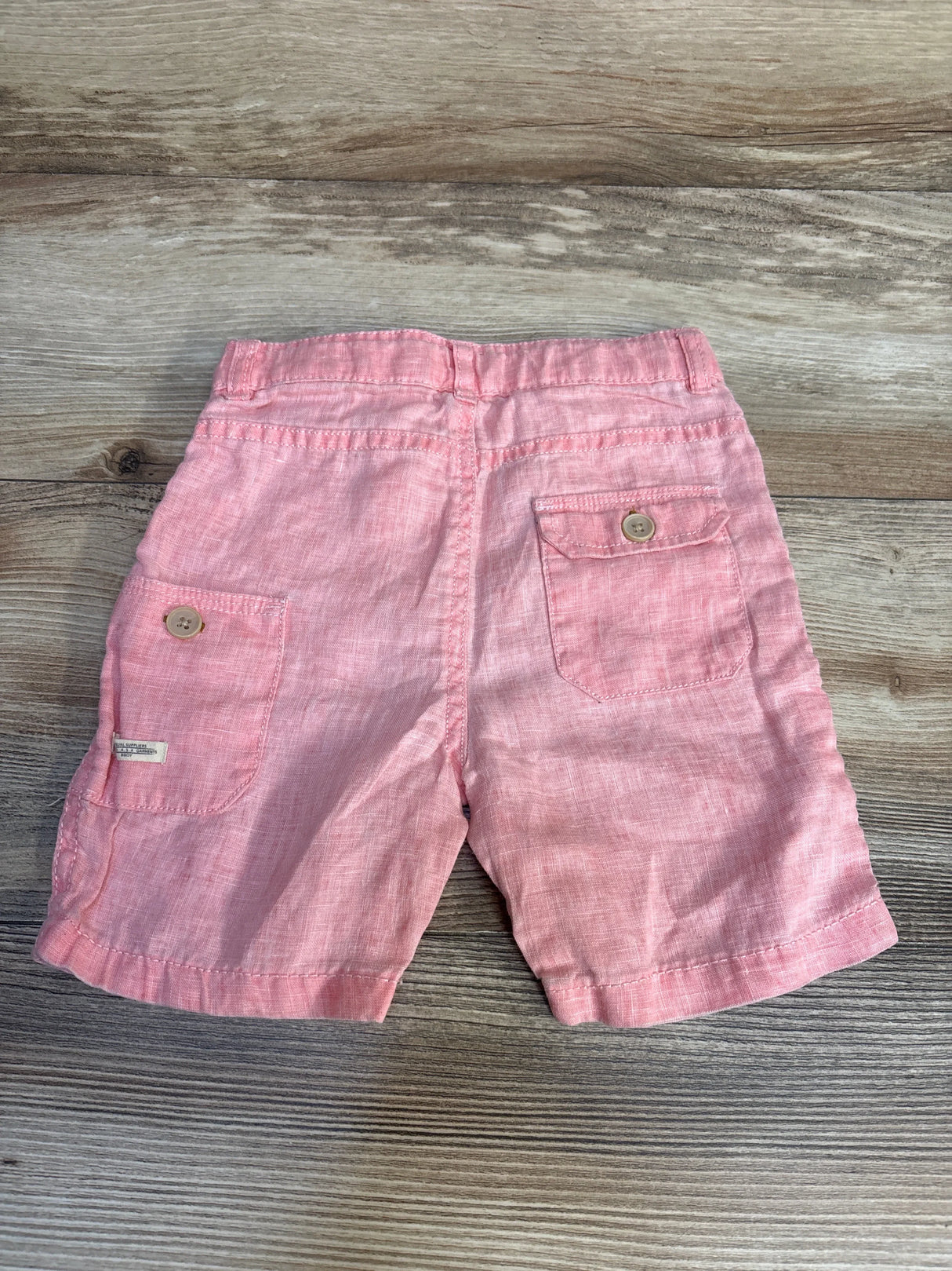 Pink linen toddler shorts with back pockets and buttons on wood background