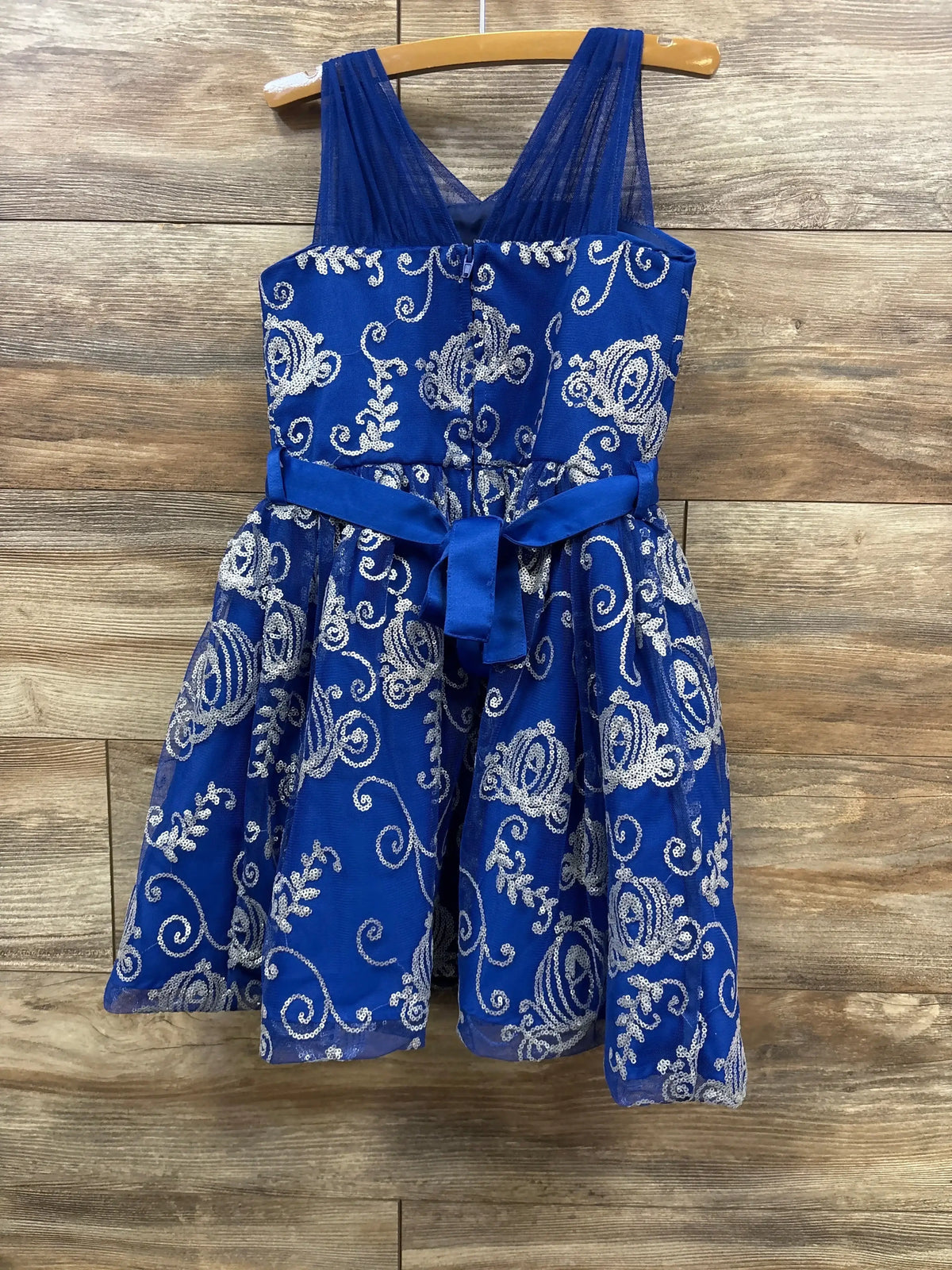 Front view of Cinderella sequin party dress, royal blue with silver sequin swirls and tied sash on wood background