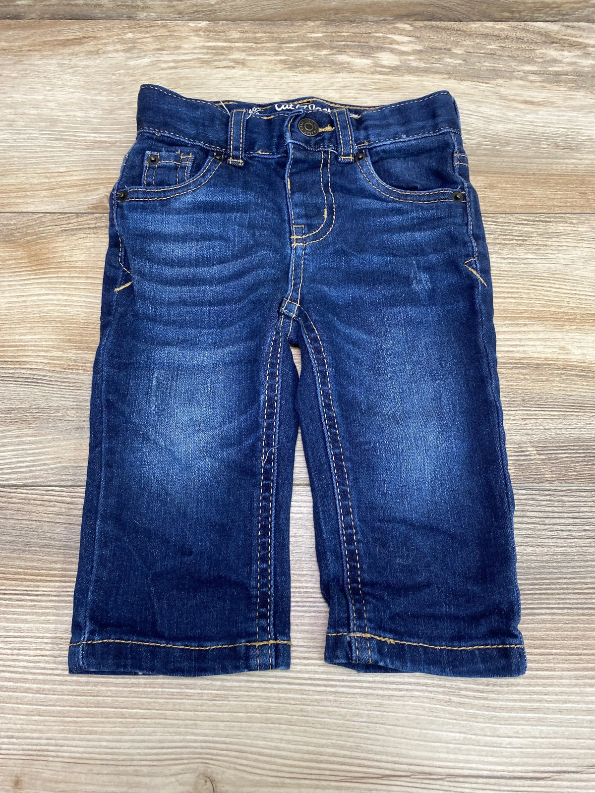 Flat lay of toddler straight-leg blue denim jeans size 12 months showing front pockets and contrast stitching on wood background
