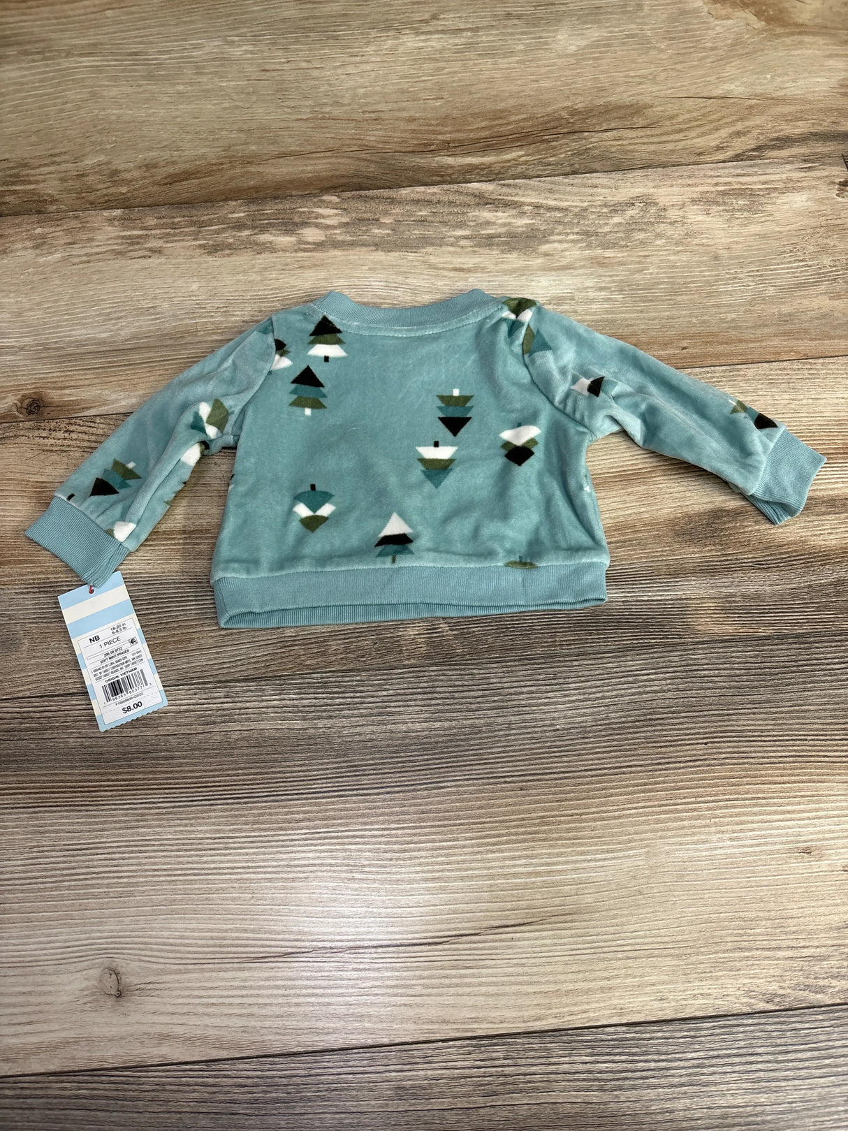 Baby long sleeve blue top with tree print, displayed on wood background with price tag