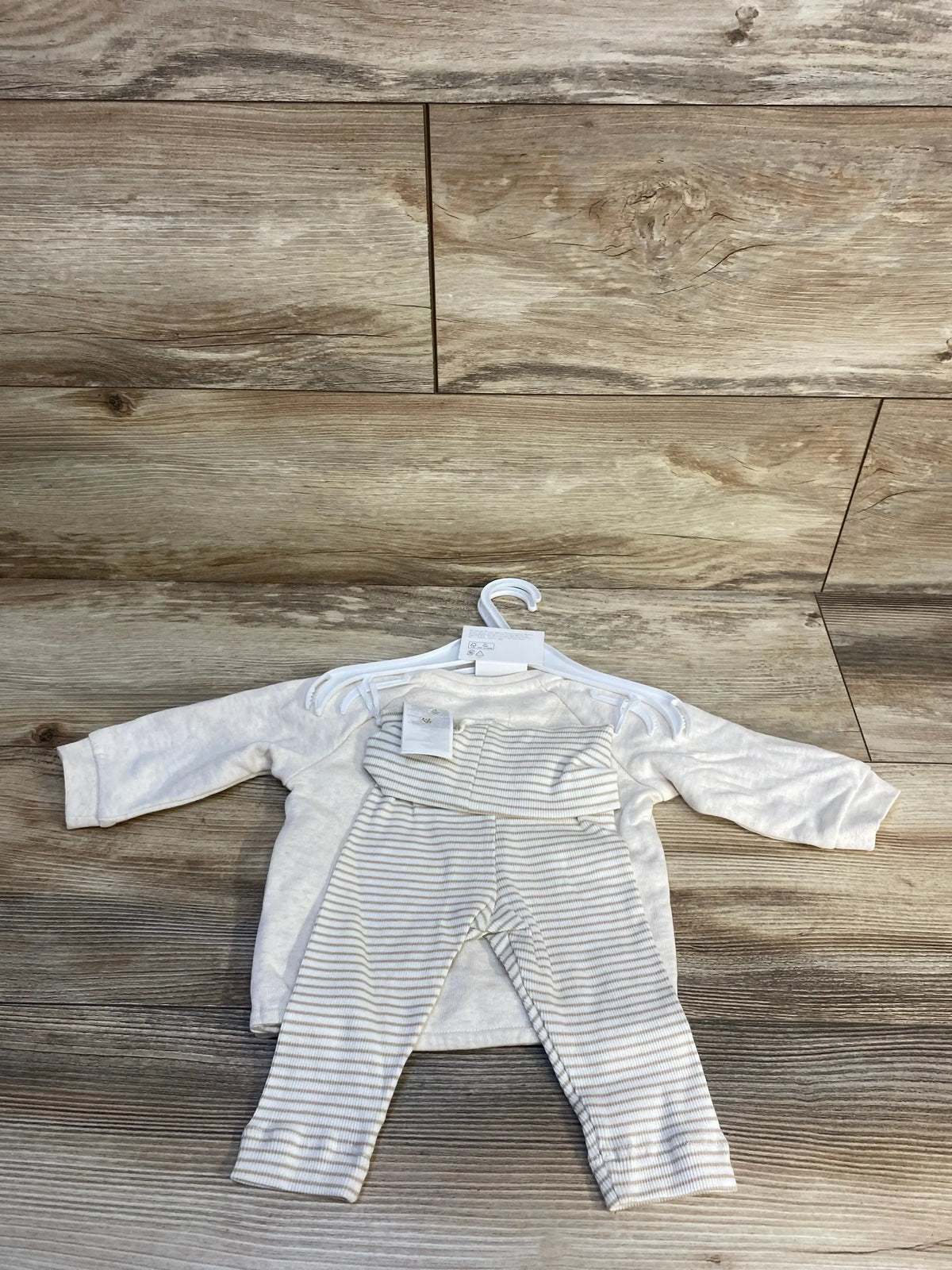 Flat lay of H&M 3-piece taupe baby shirt set size 3 months showing long-sleeve cream top with ‘hello world’ print and striped pants on wooden floor