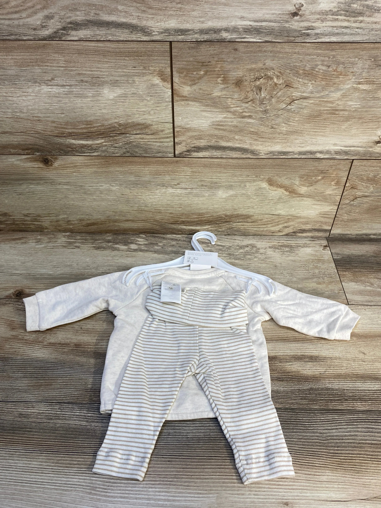 Flat lay of NEW H and M three piece Hello World set in taupe with long sleeve top and striped pants on hanger on wood plank floor