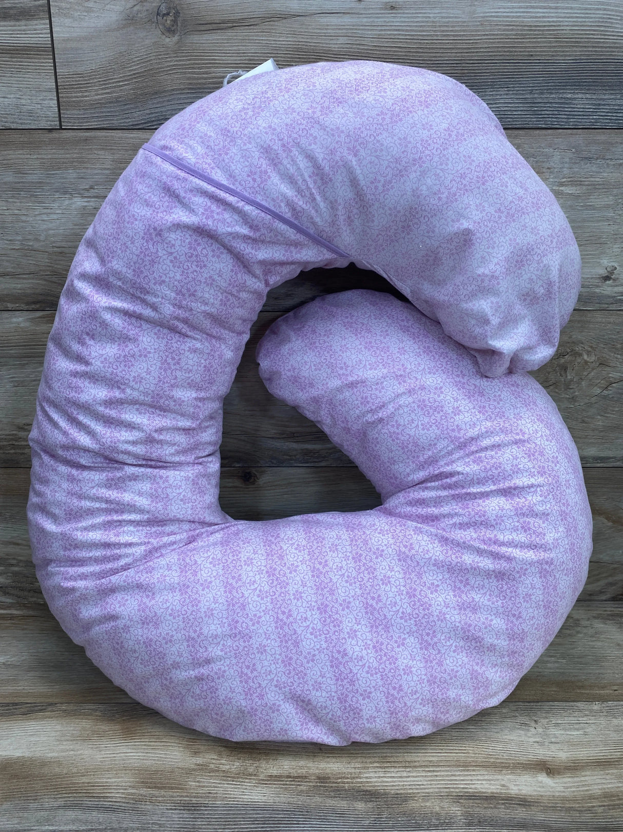 Top-down view of Leachco Snoogle Mini support pillow showing purple patterned zippered cover and C-shaped contour on wood floor