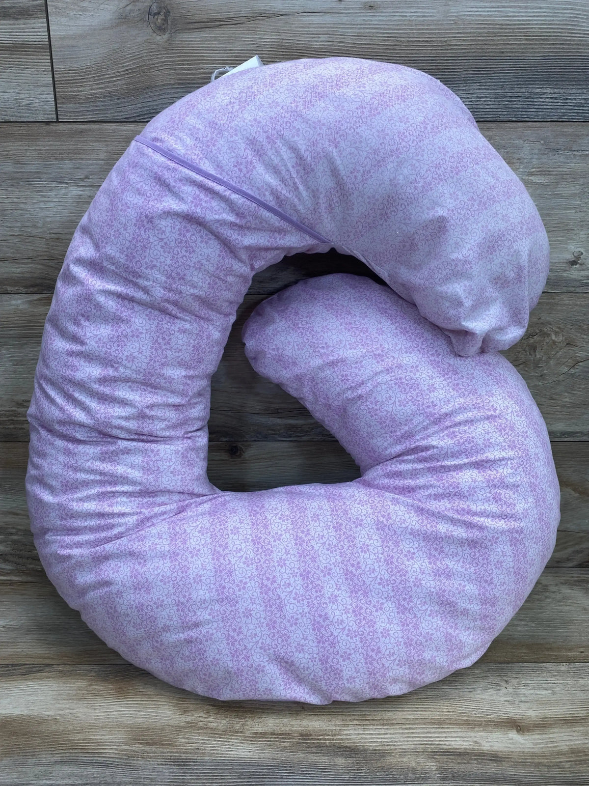 Top-down view of Leachco Snoogle Mini support pillow showing purple patterned zippered cover and C-shaped contour on wood floor