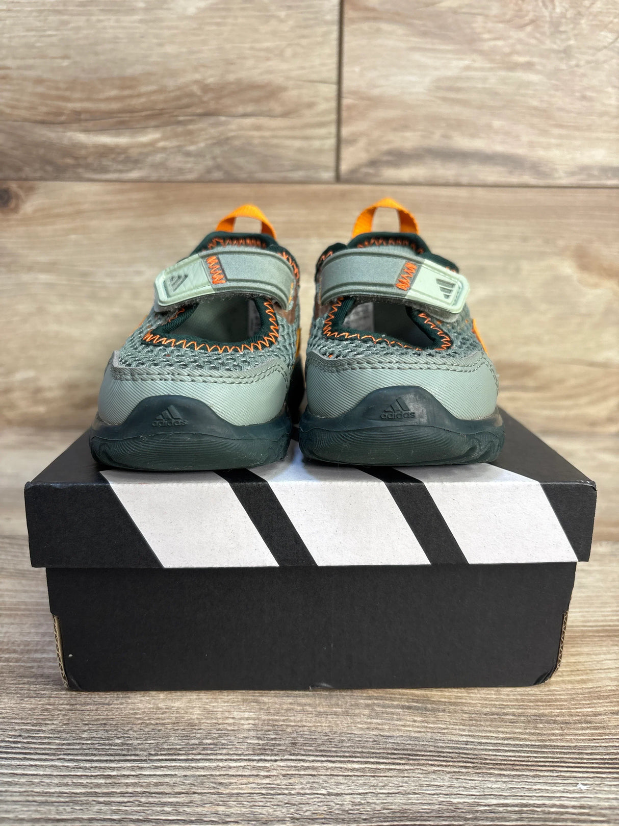 Kids grey and orange Adidas shoes with velcro straps on a shoe box, wood background