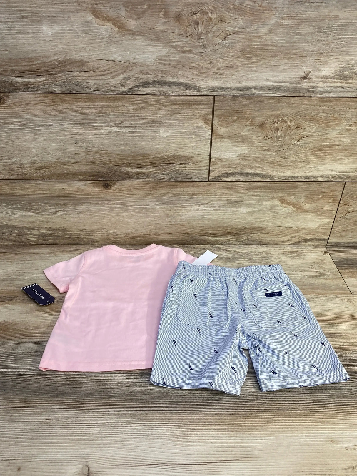 Flat lay of Nautica baby 2-piece: pink tee and blue striped shorts with elastic waist on wood