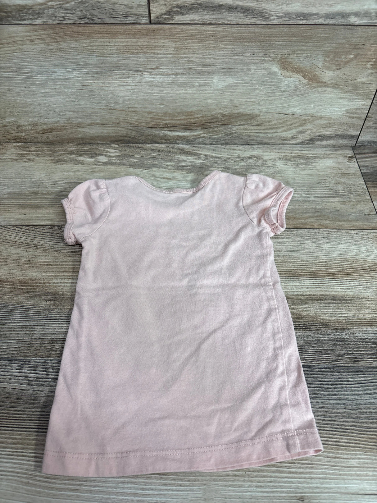 Back view of girls' pink Beautees shirt (size 3T) showing puff sleeves and crew neck laid flat on wood floor