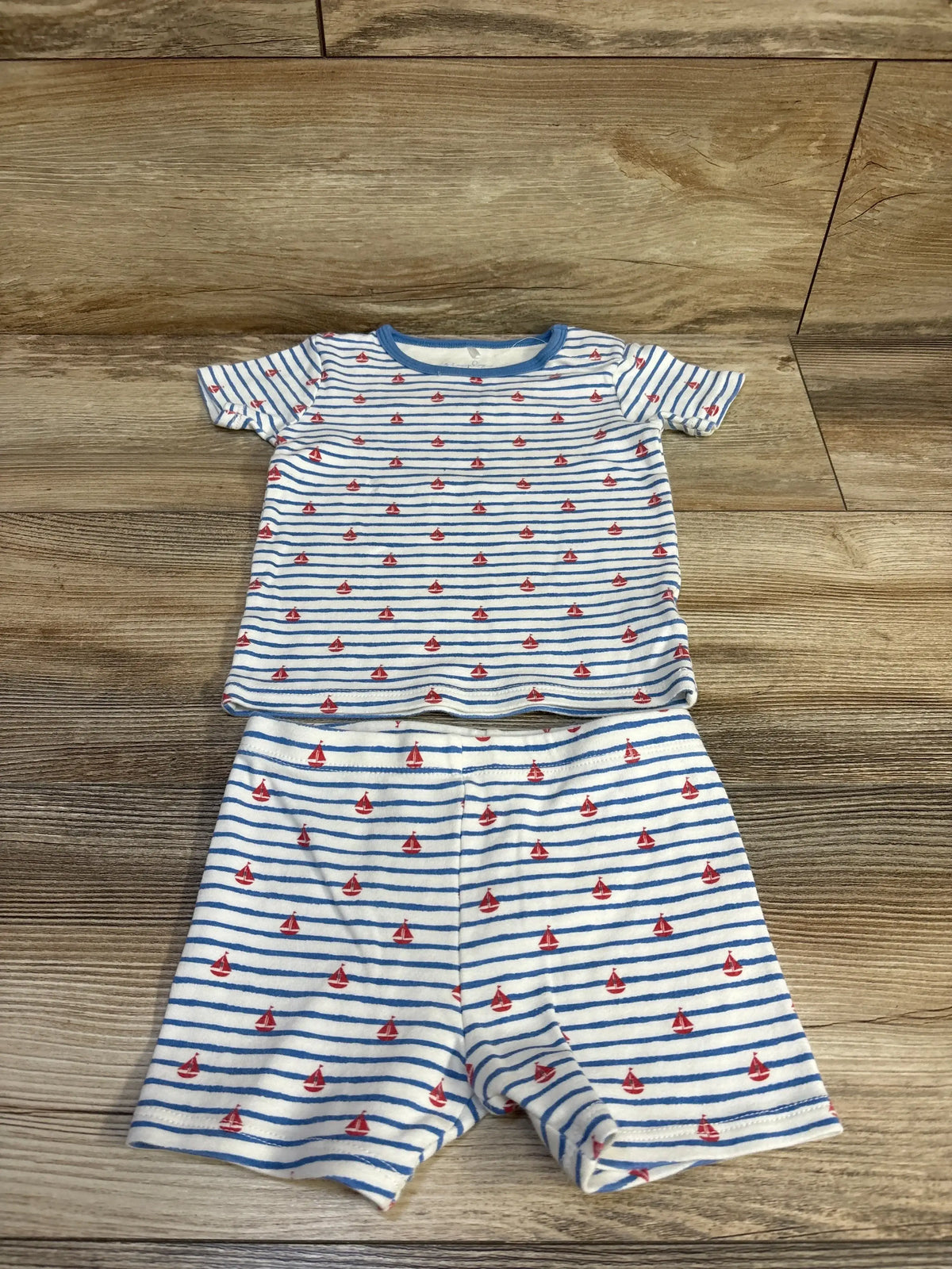 Flat lay of Magnetic Me 2-piece toddler pajama set, size 2T, white with blue stripes and red sailboat print, on wood floor