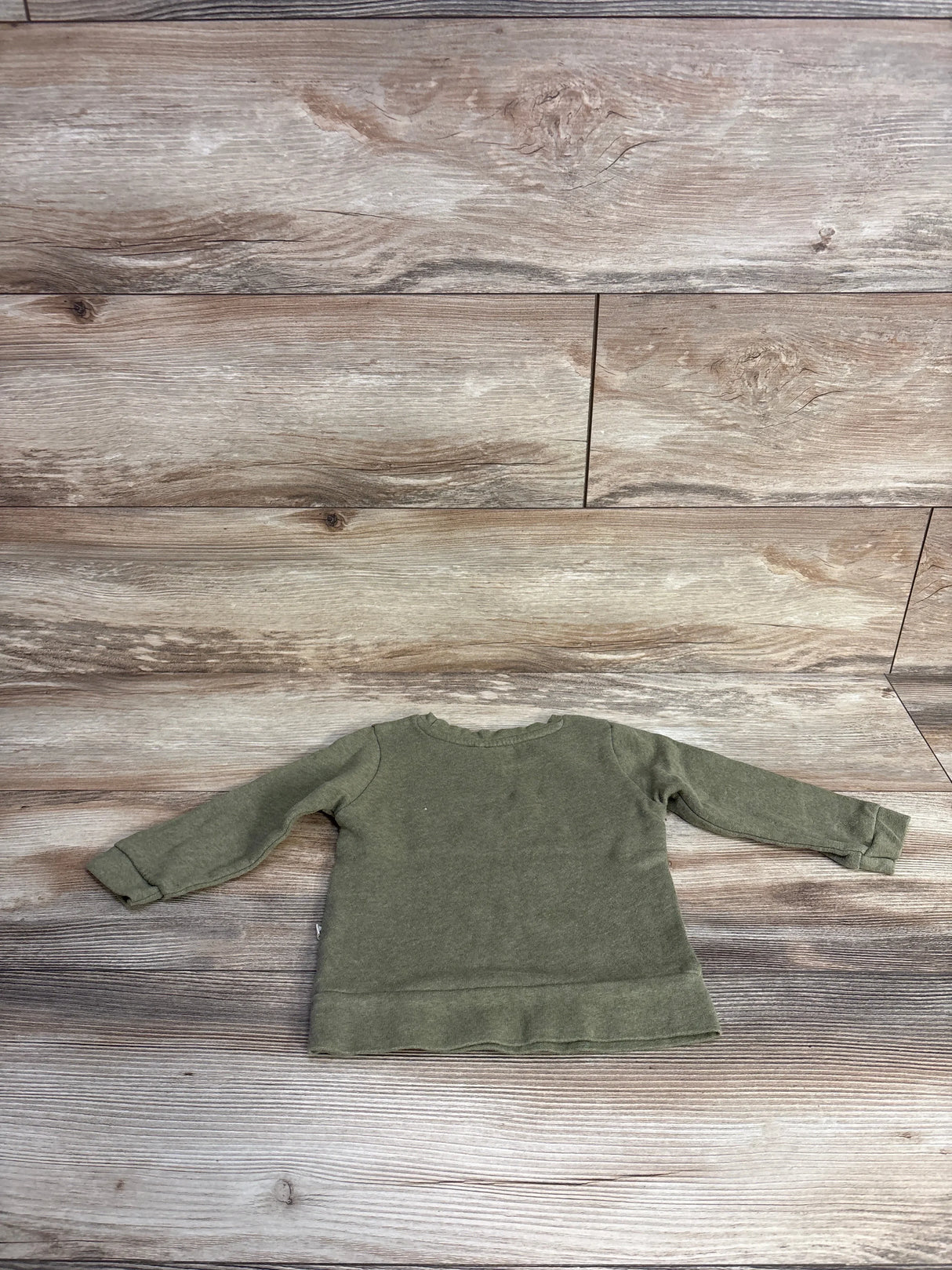 Front view of green toddler pullover sweater in size 12 months showcasing ruffled hem and long sleeves on wood plank floor