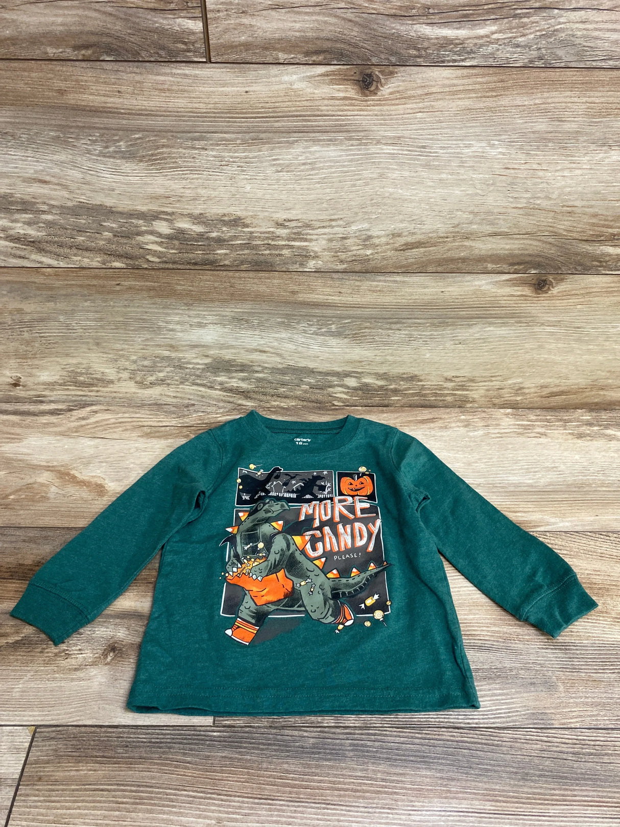 Green toddler long sleeve shirt with dinosaur Halloween graphic saying 'More Candy Please!' on wood floor