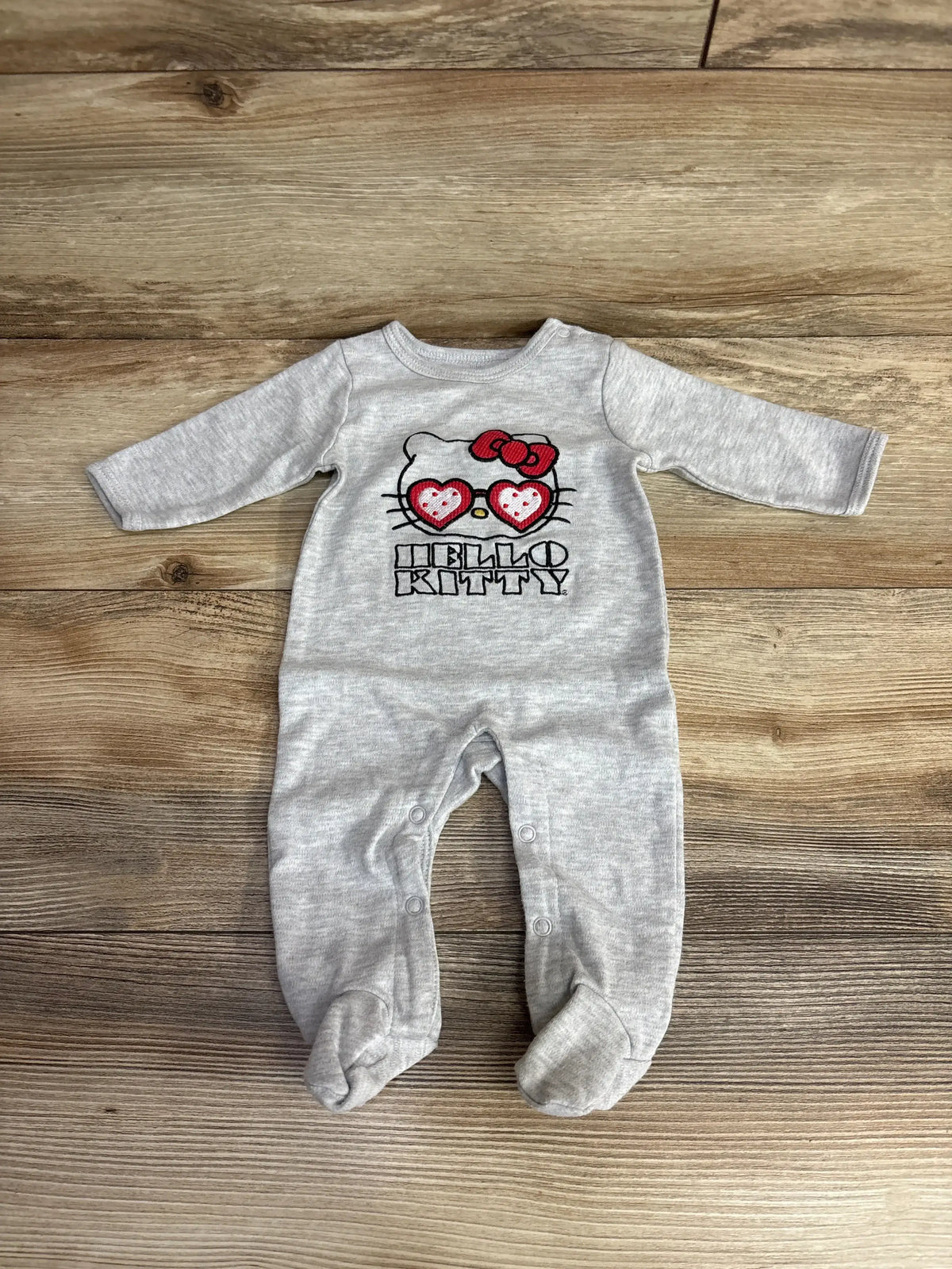 Gray Hello Kitty baby footed sleeper with heart glasses, long sleeves on wooden background