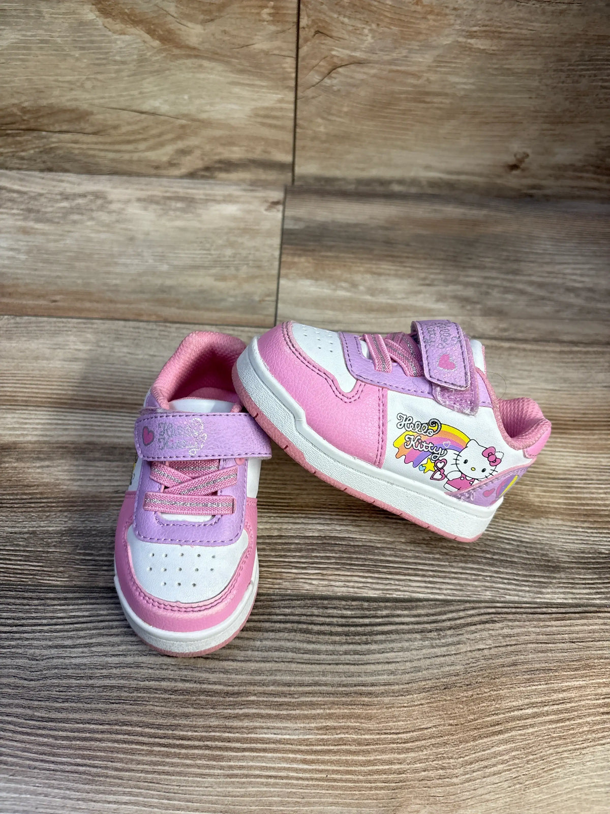 Front three-quarter view of toddler Hello Kitty Velcro sneakers in pink and white with Hello Kitty side graphic on wood floor