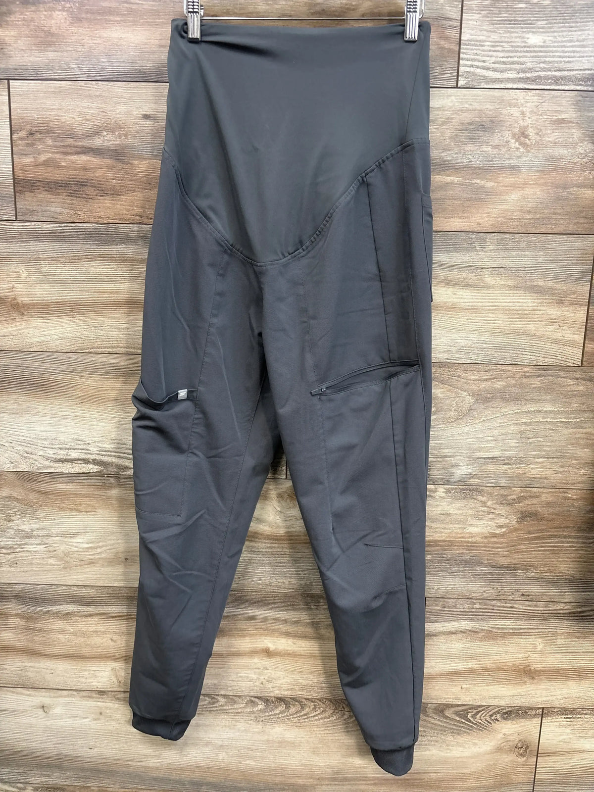 Front view of maternity scrub joggers showcasing high rise over belly panel, side cargo and zip pocket with wood plank background