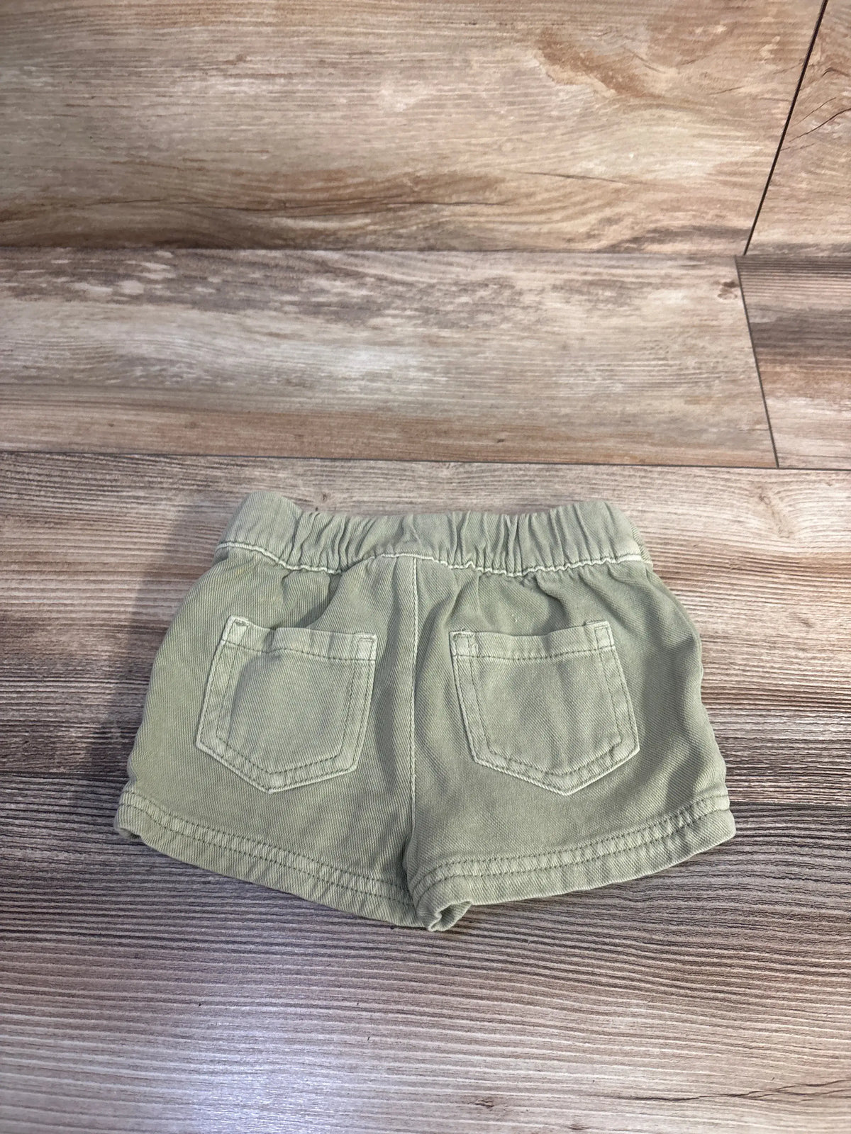 Back view of green Cat & Jack toddler shorts showcasing two back pockets and elastic waistband on a wood-look floor