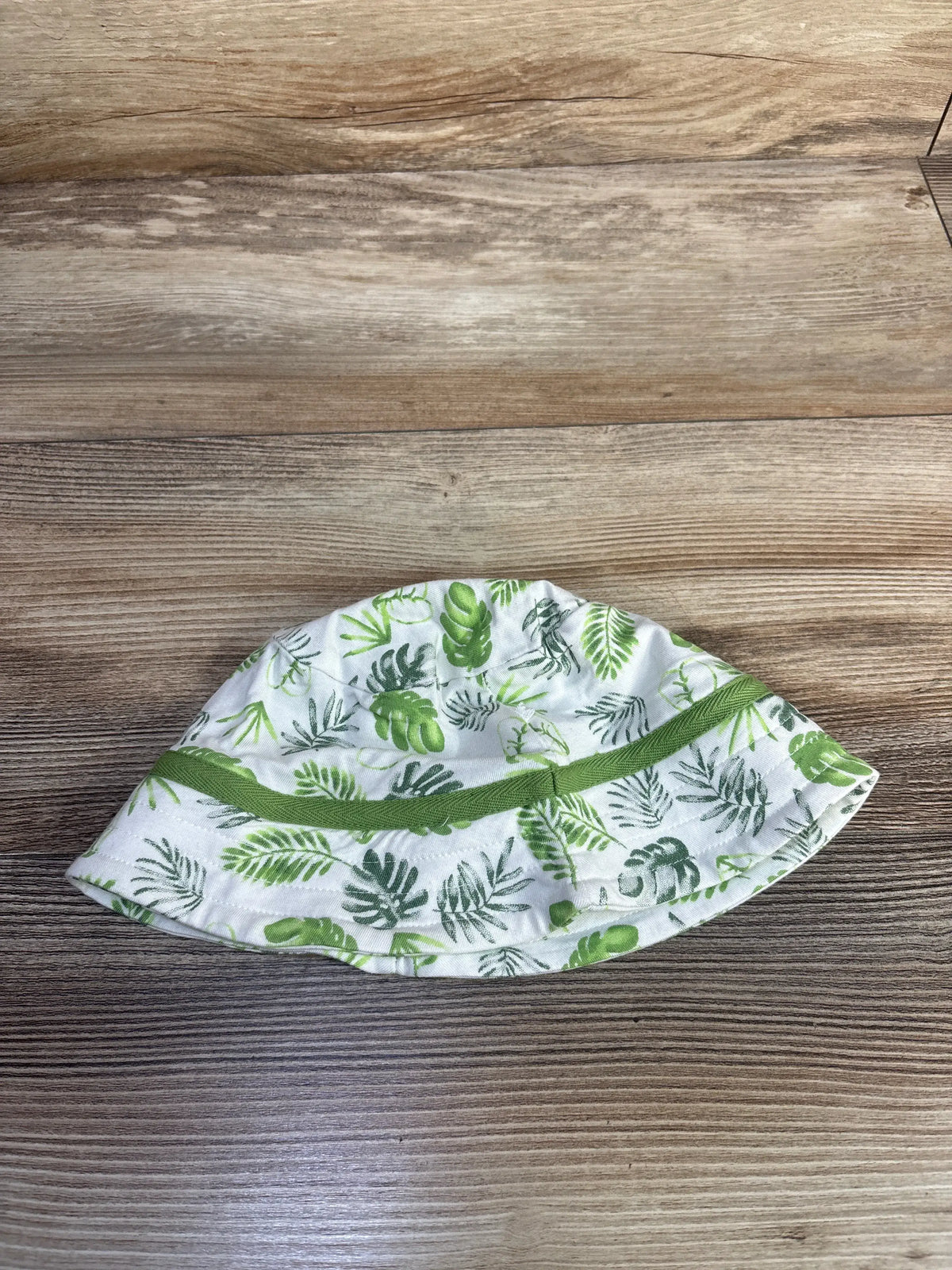 Overhead view of white tropical bamboo bucket hat in size 9 months with green leaf print and wide brim on wood grain