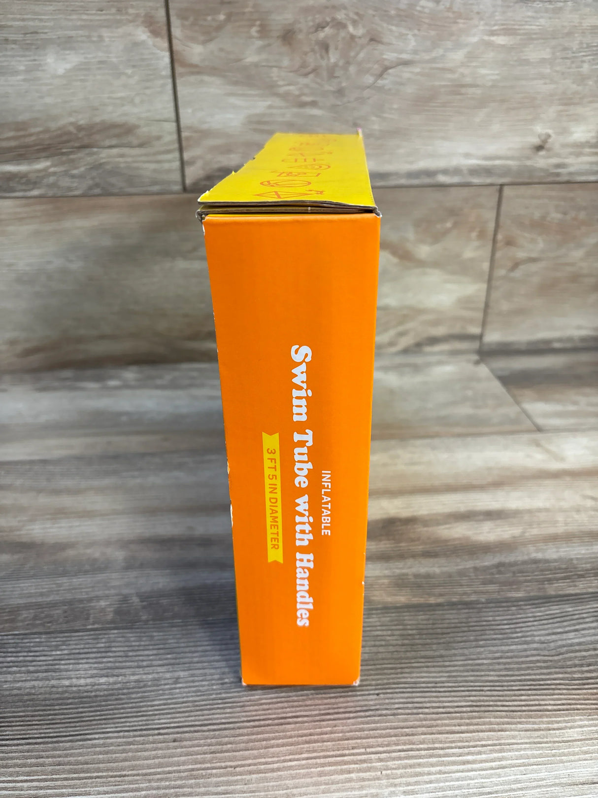 Side view of Sun Squad Swim Tube with Handles Rainbow 41in orange box showing Inflatable 3FT 5IN Diameter label on wood plank floor