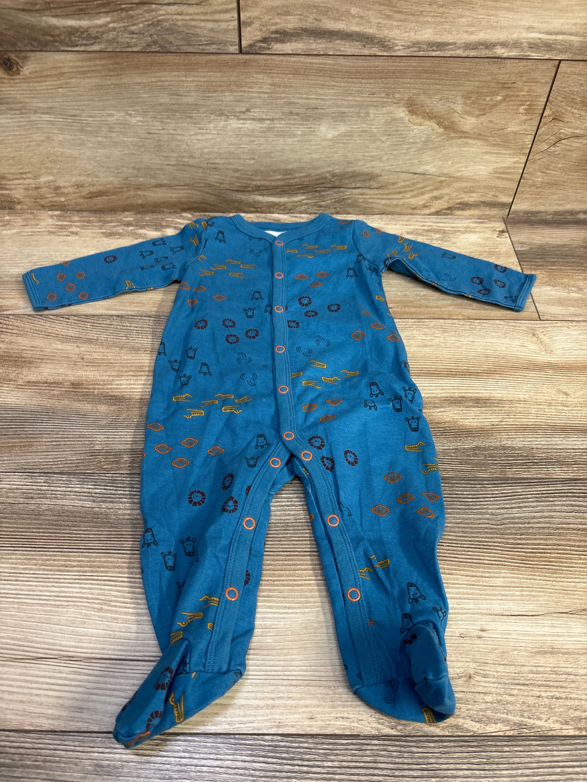 Flat lay of blue Carter’s footed snap sleeper (6M) showing front snap closure and small animal prints on wood background