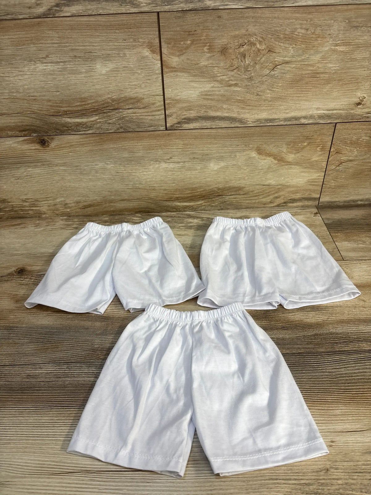 Flat lay of three white baby bike shorts showcasing elastic waistbands and mid-thigh length on wood floor