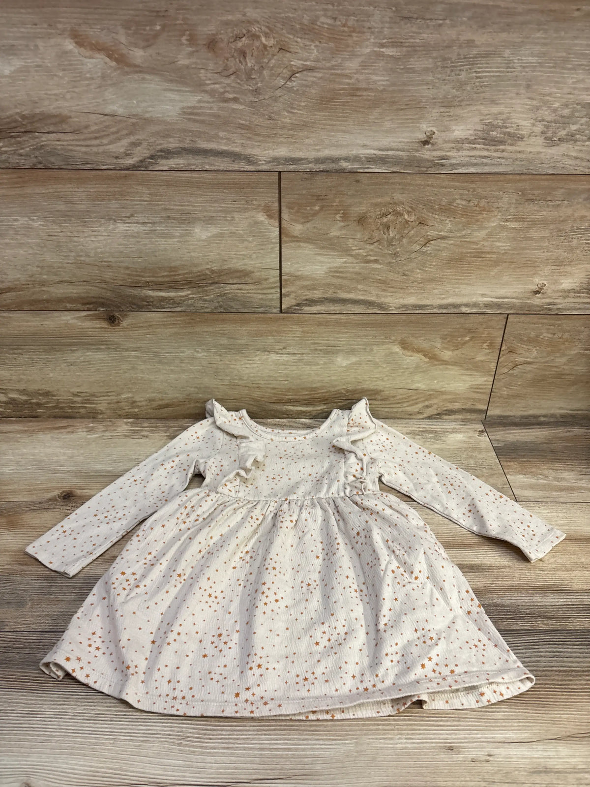 Front view of Cat & Jack beige long sleeve dress showcasing ruffled shoulders and star print with wood flooring background