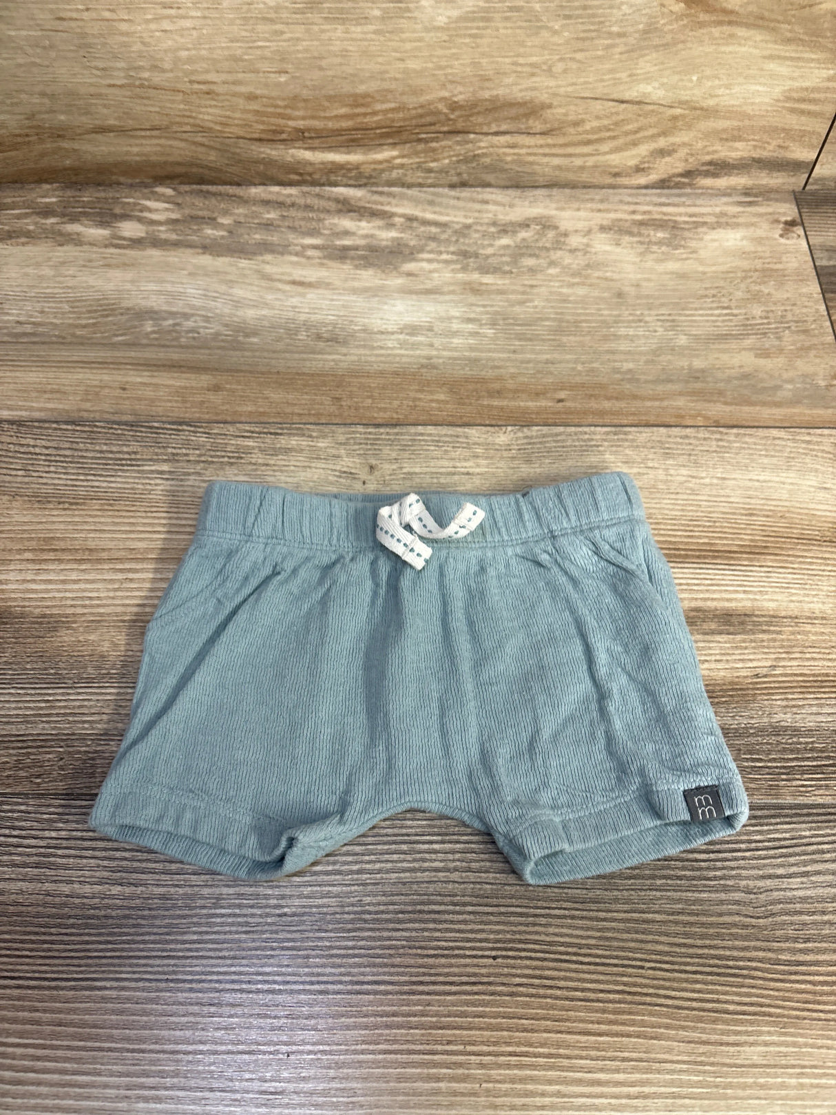 Front view of newborn blue Modern Moments drawstring shorts with elastic waist, white tie, ribbed fabric on wood