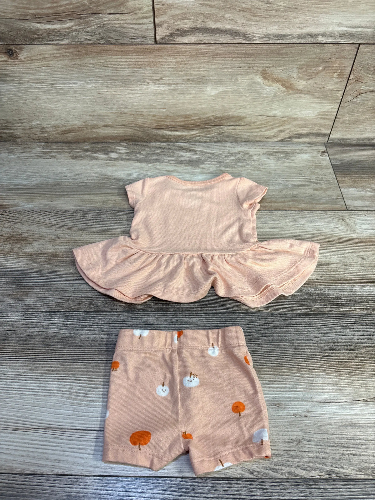 Top-down view of Cat and Jack pumpkin peplum top and shorts set showing flared peplum and pumpkin-print shorts on wood grain