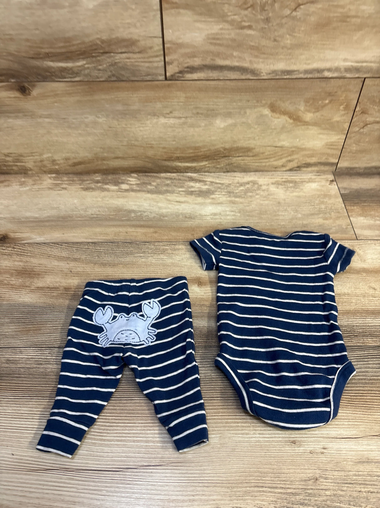 Flat lay of Carter’s newborn 2-piece navy-and-white striped bodysuit and pants showcasing crab applique on back on wood