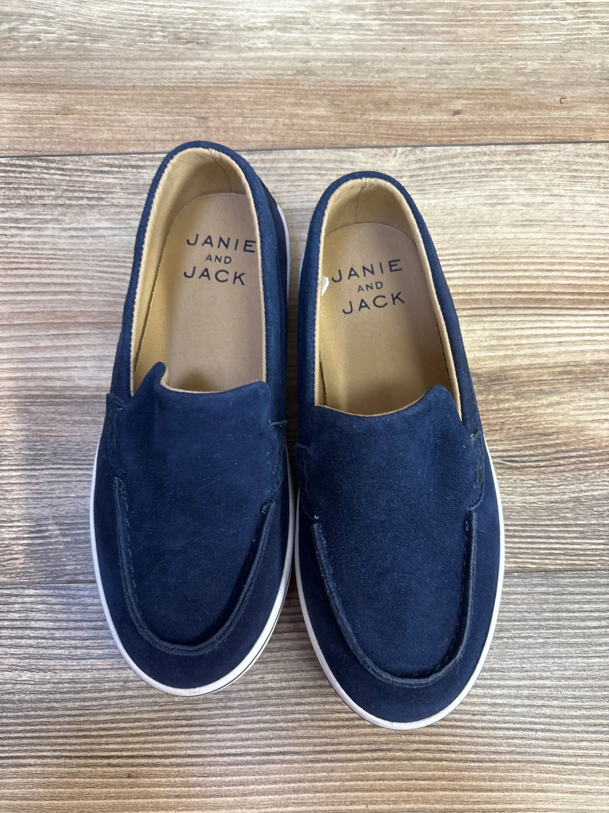 Top view of Janie & Jack blue suede slip-on sneakers showing the easy slip-on design on a wood-grain background