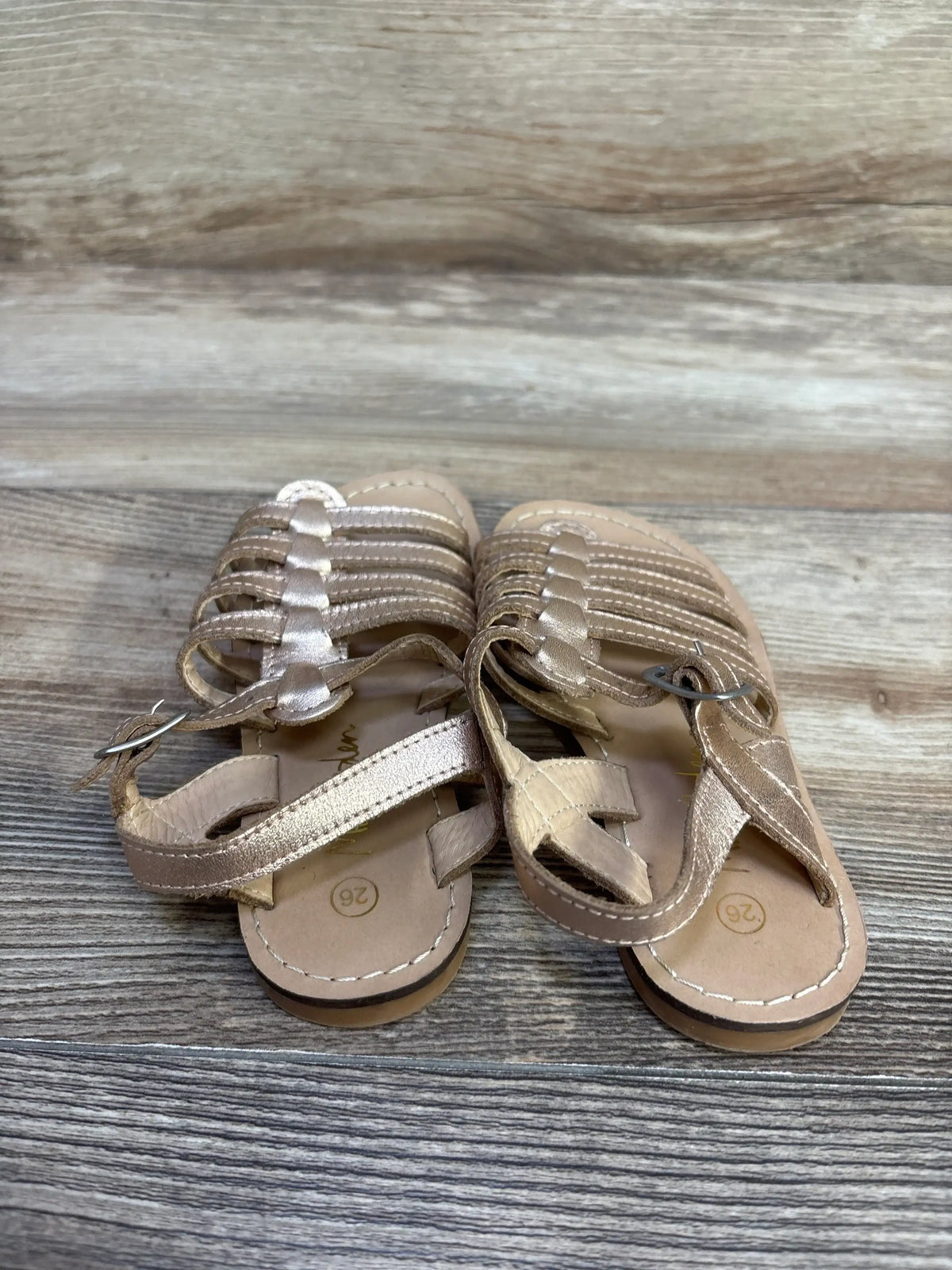 Top-down view of Mini Boden gold gladiator sandals, size 9C (marked 26), multi-strap upper with toe loop and ankle buckle on wood floor