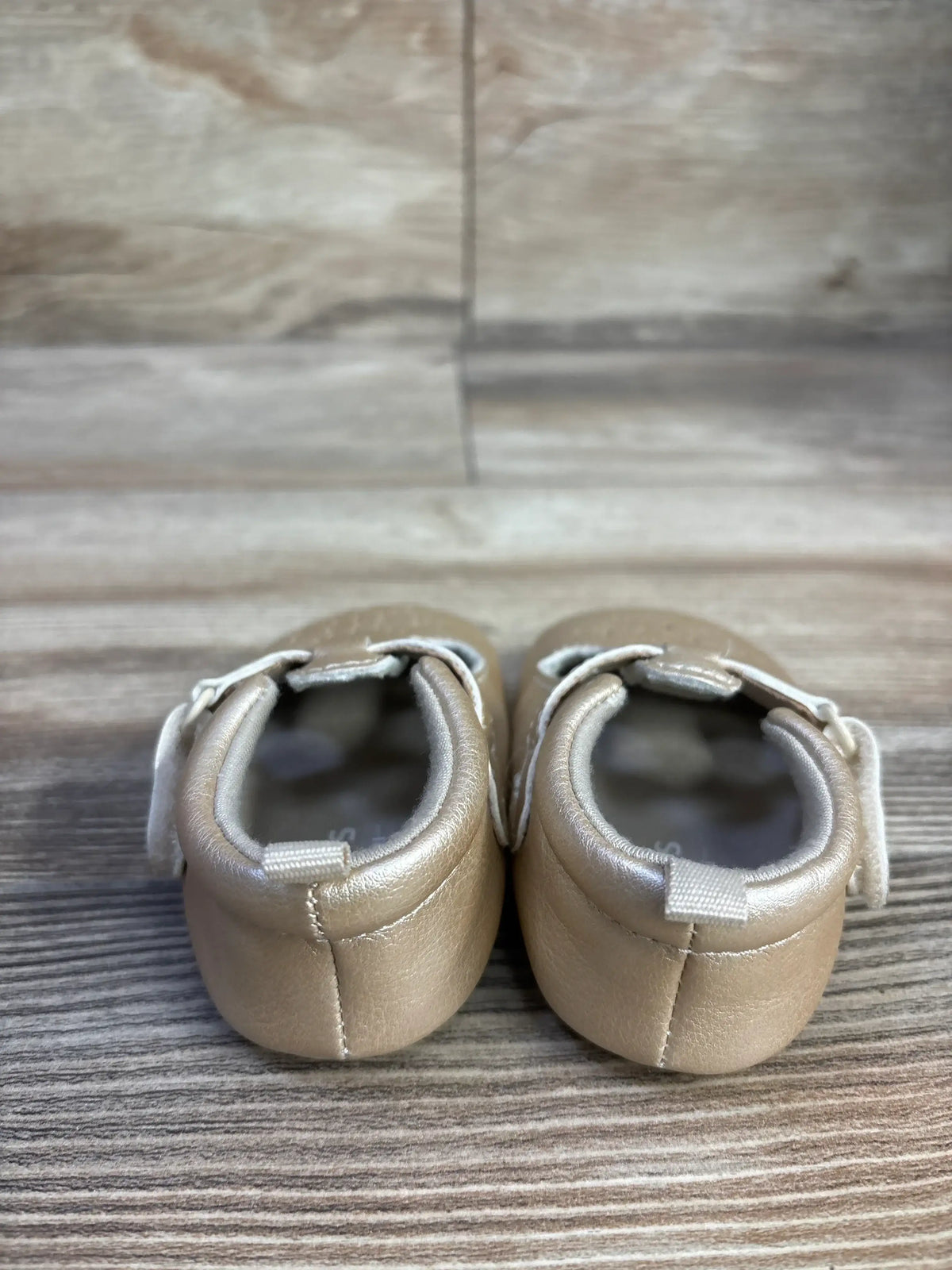 Rear view of Just One You Stella gold sandals showing hook-and-loop straps on a wood surface