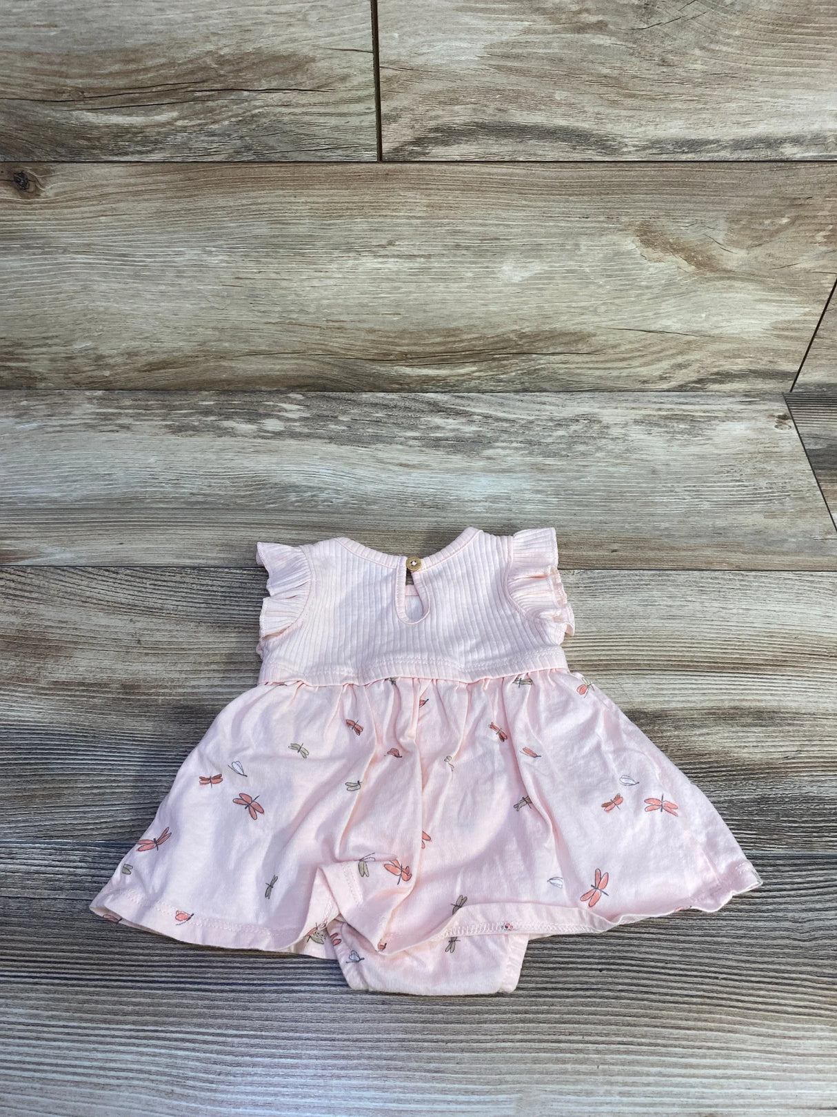 Flat lay of newborn pink ribbed bodysuit dress with flutter sleeves and dragonfly print skirt on wood plank background