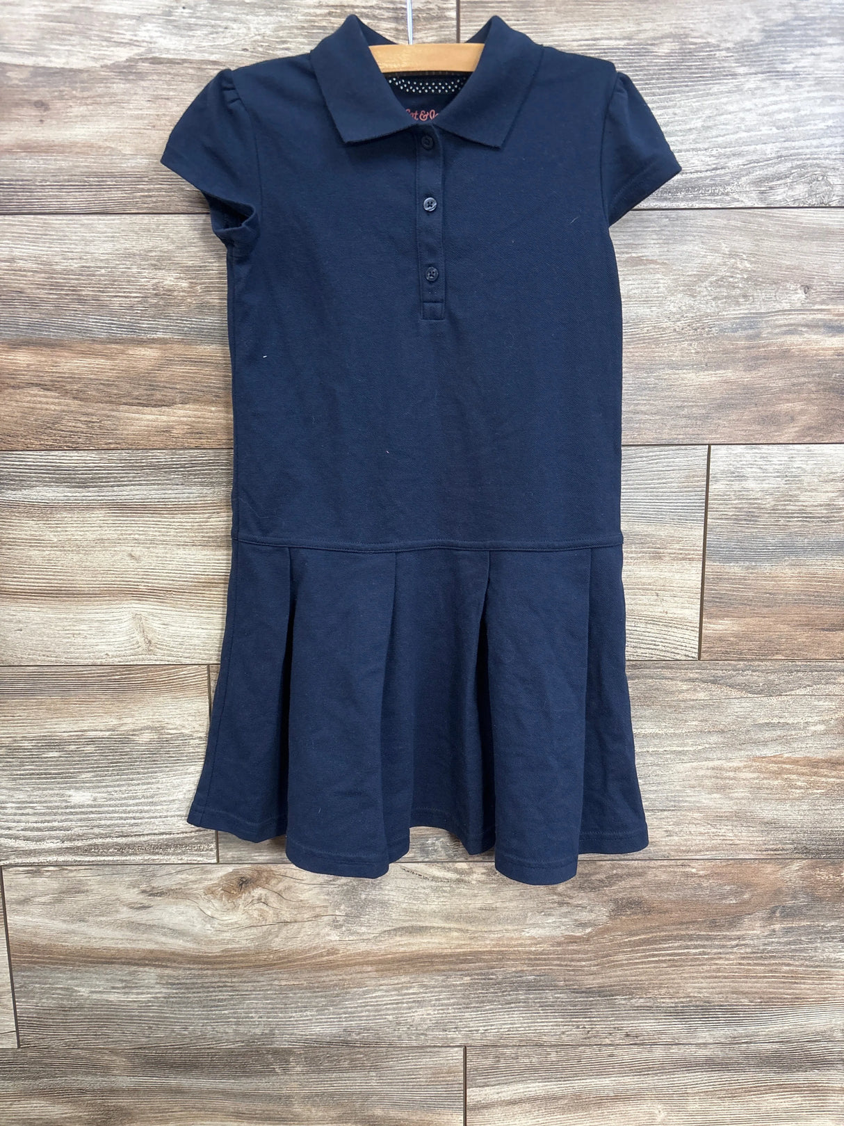 Front view of navy girls pleated school dress with polo collar, three button placket and short sleeves on wooden hanger