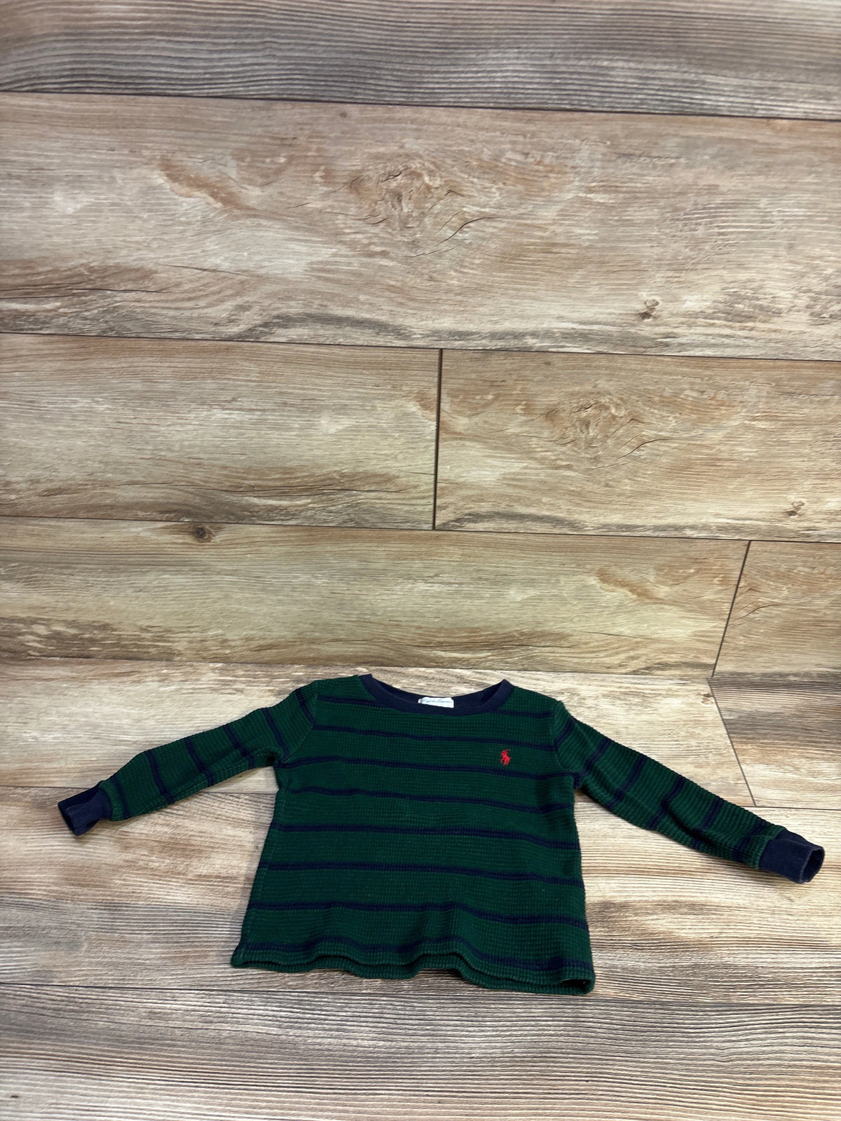 Flat lay of Ralph Lauren green waffle-knit long-sleeve shirt with navy stripes and red pony logo, size 18M on wood floor