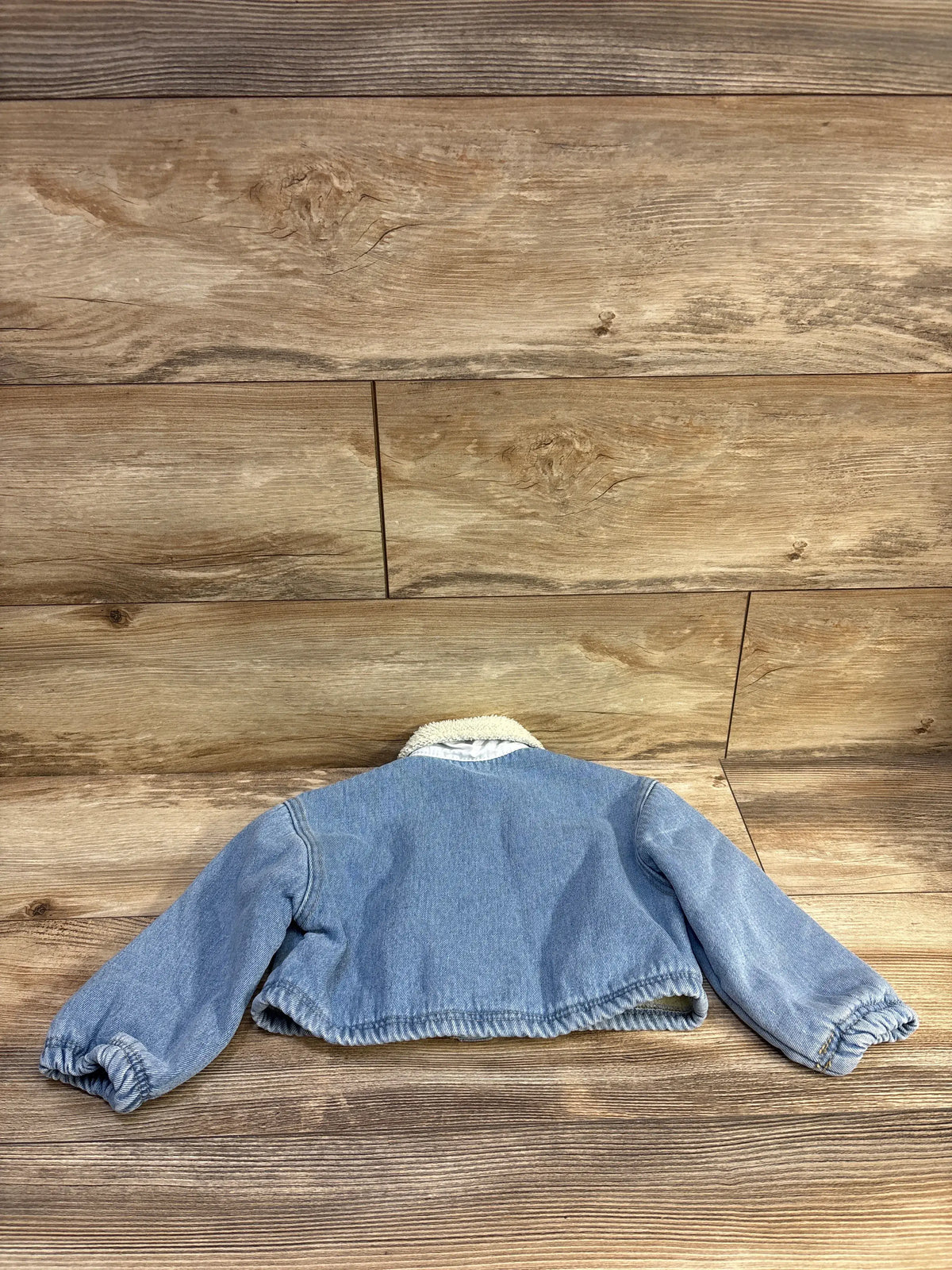 Back view of Cozy Pixies blue sherpa-lined denim jacket, size 2-3T, with sherpa collar and elastic cuffs on wood floor