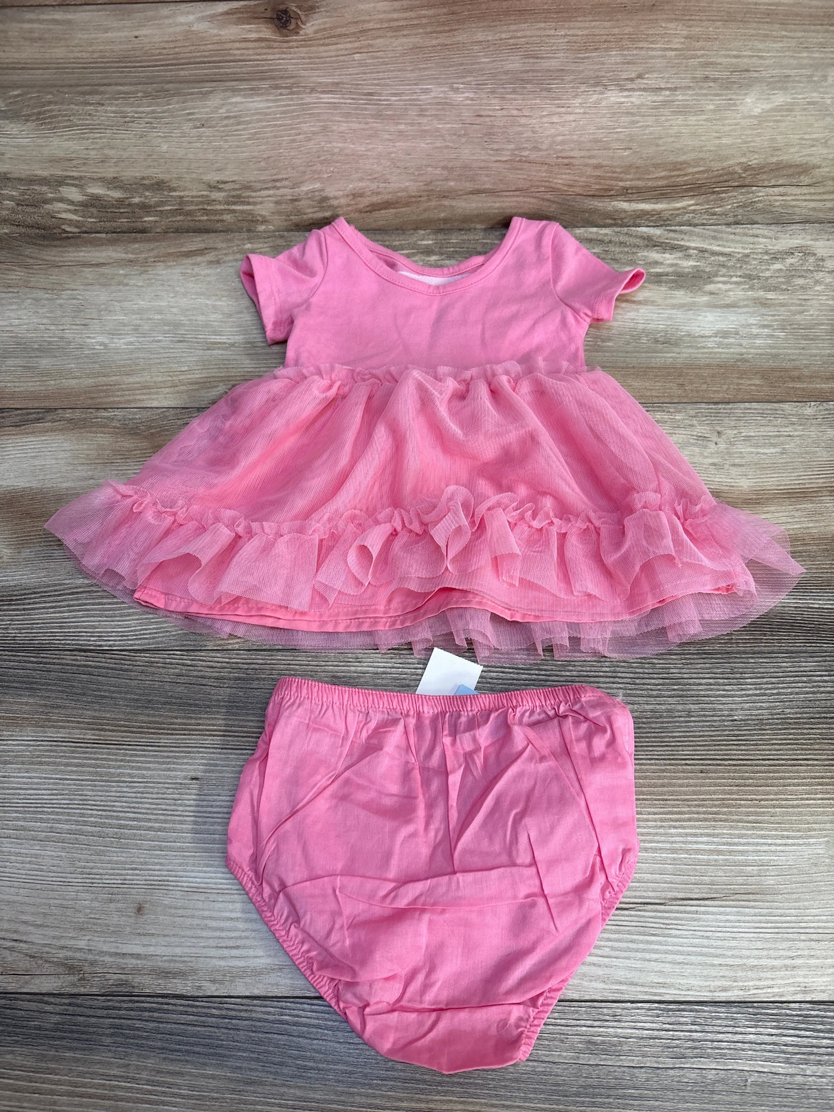 Pink baby dress with ruffled tulle skirt and matching bloomers on wooden surface