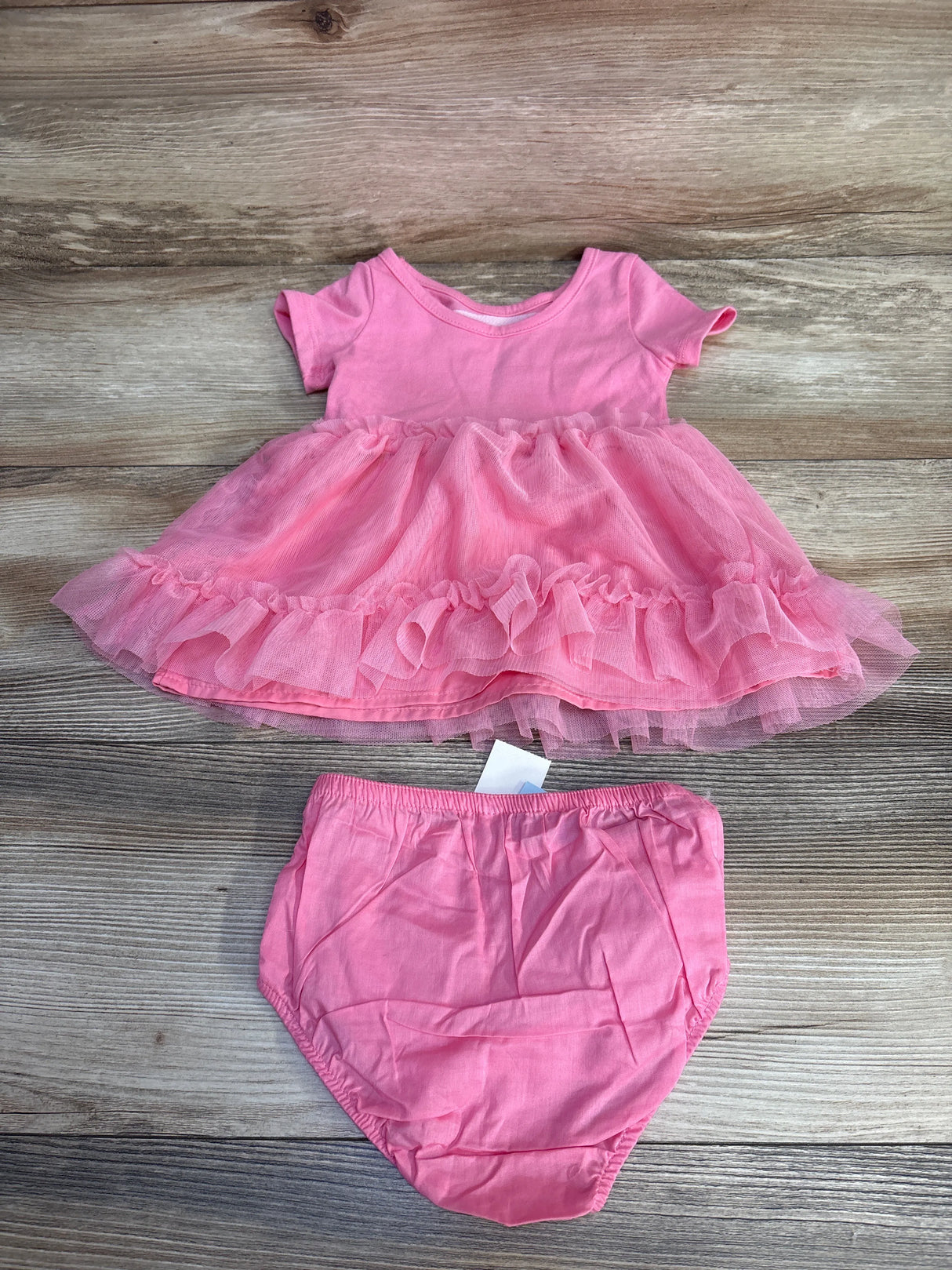 Pink baby dress with ruffled tulle skirt and matching bloomers on wooden surface