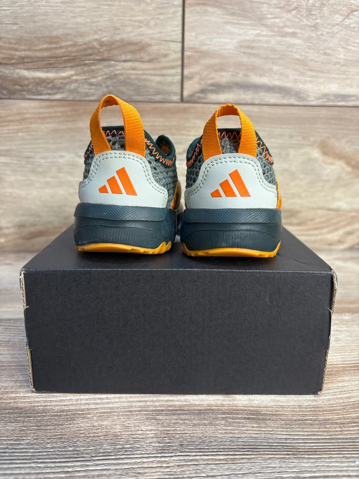 Rear of Adidas Summerflex I toddler sandals with gray-green knit, orange heel pull tabs and orange logo, on a black box and wood background
