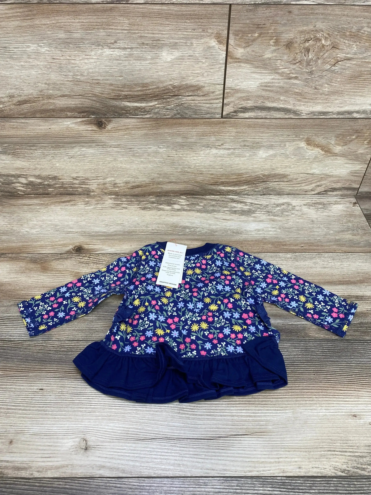 Front view of Cat & Jack navy floral peplum adaptive baby shirt (3–6M) showcasing ruffled hem and long sleeves on wood background