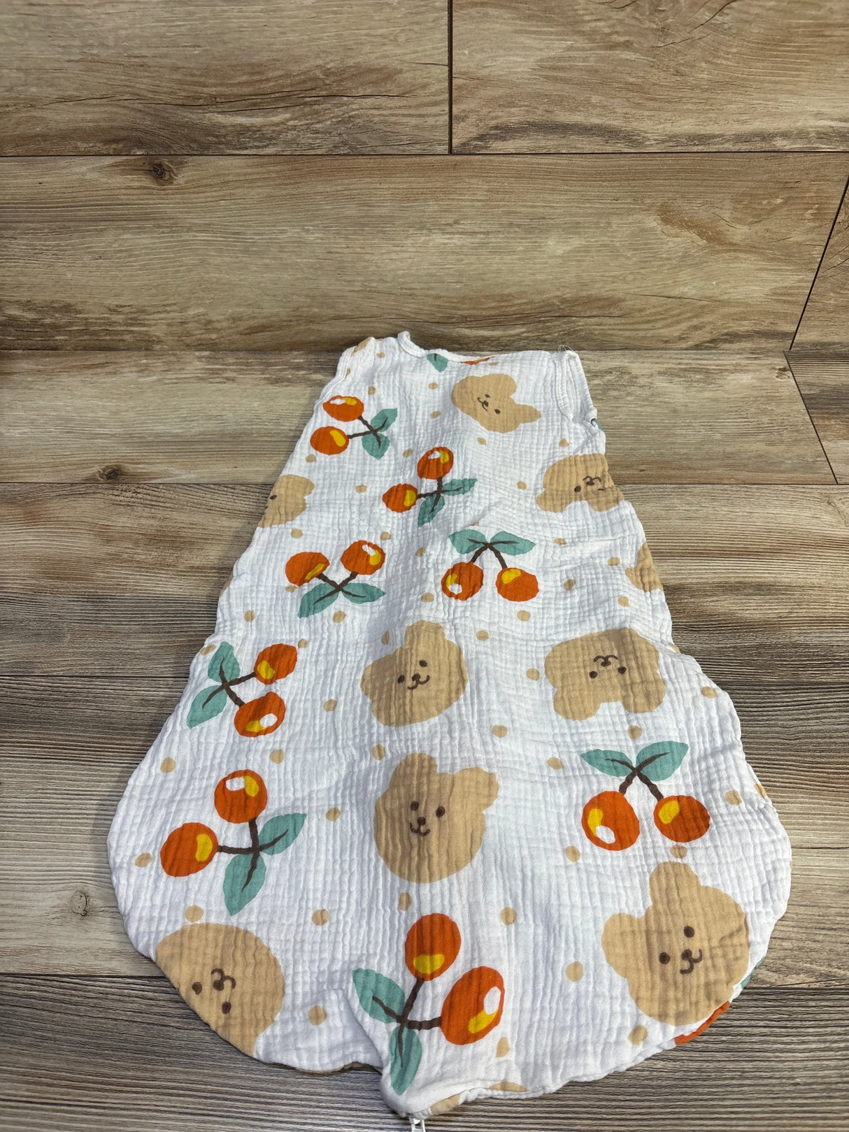 Flat lay of size Small (0-6M) white gauze sleep sack showing orange cherry and tan bear-face print on wood background