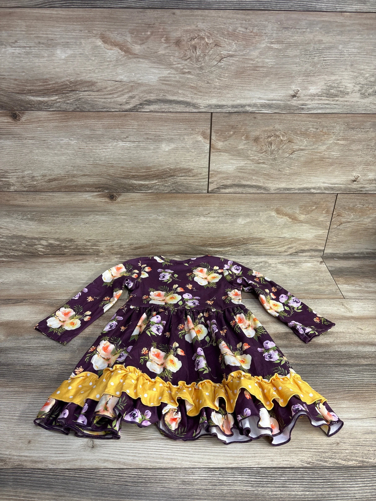 Long-sleeve toddler dress with purple floral print and yellow ruffle hem displayed on wood floor