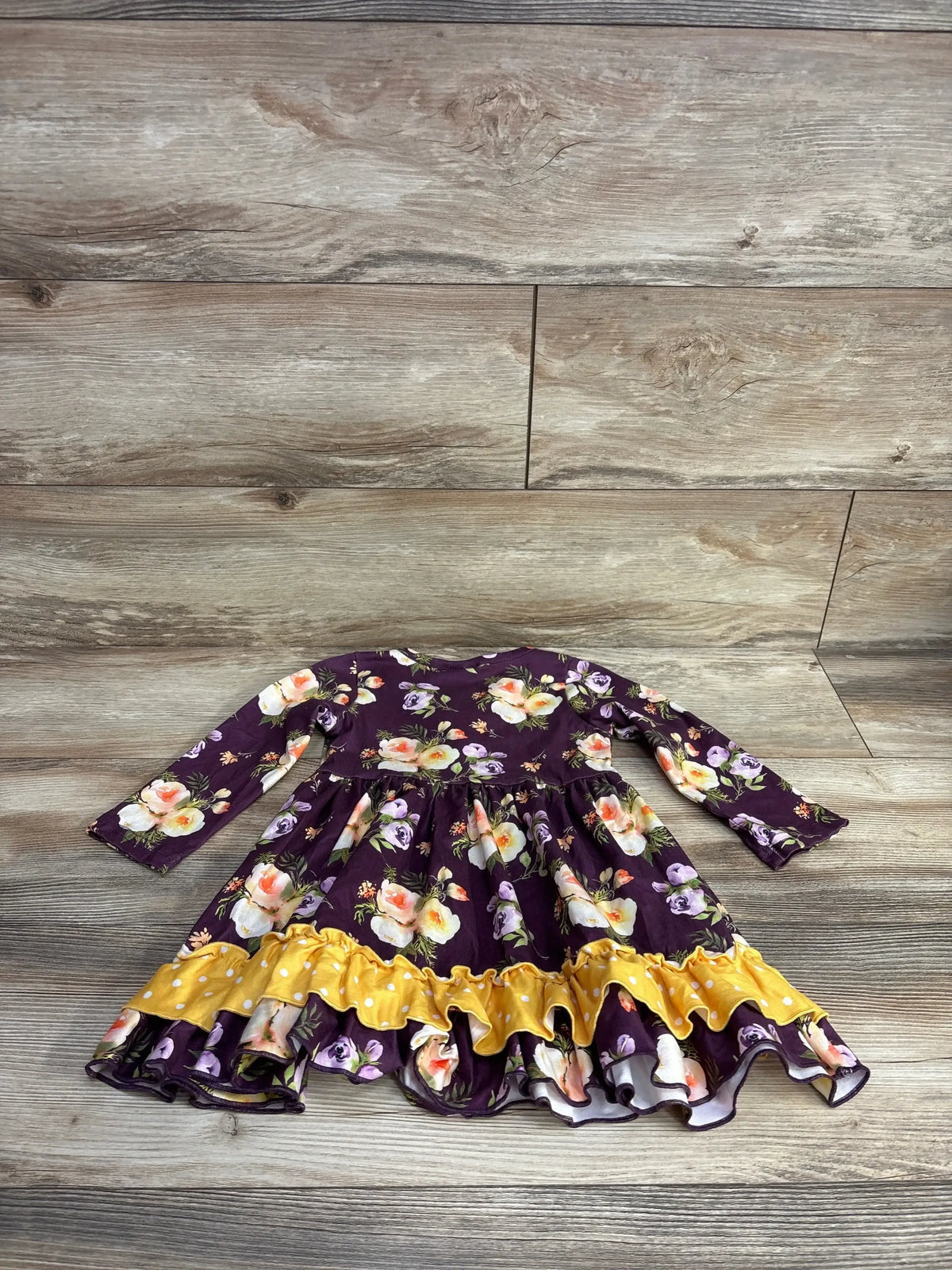 Long-sleeve toddler dress with purple floral print and yellow ruffle hem displayed on wood floor