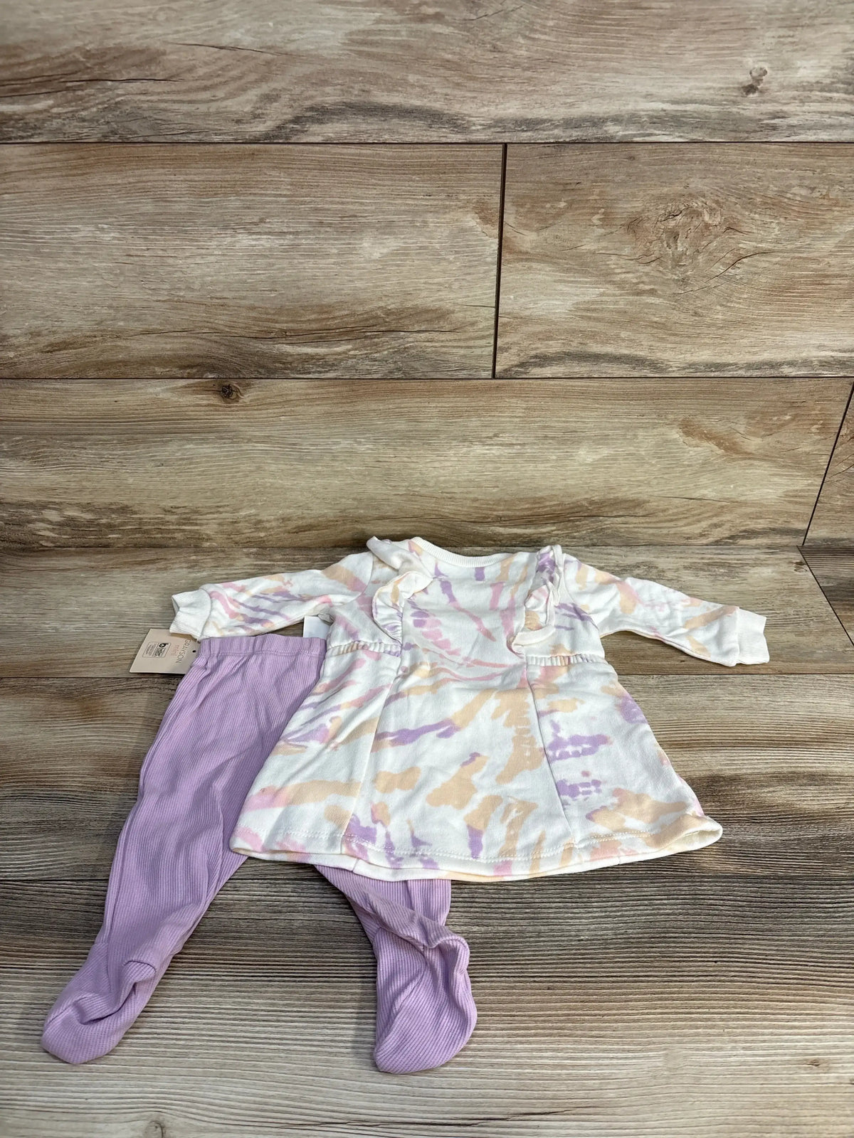 Baby outfit with pastel tie-dye dress and lavender leggings on wood background