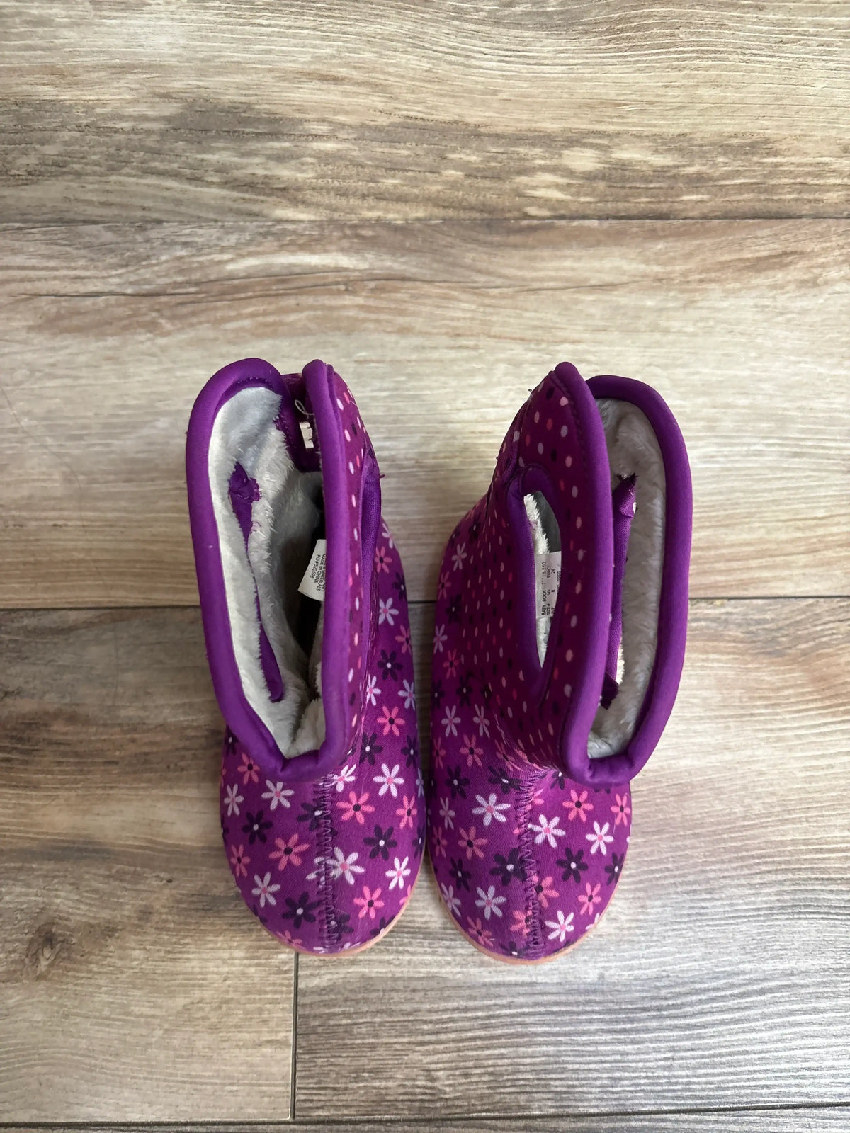 Top-down view of BOGS II toddler purple rain boots showing floral and polka-dot print and fleece lining on wood floor