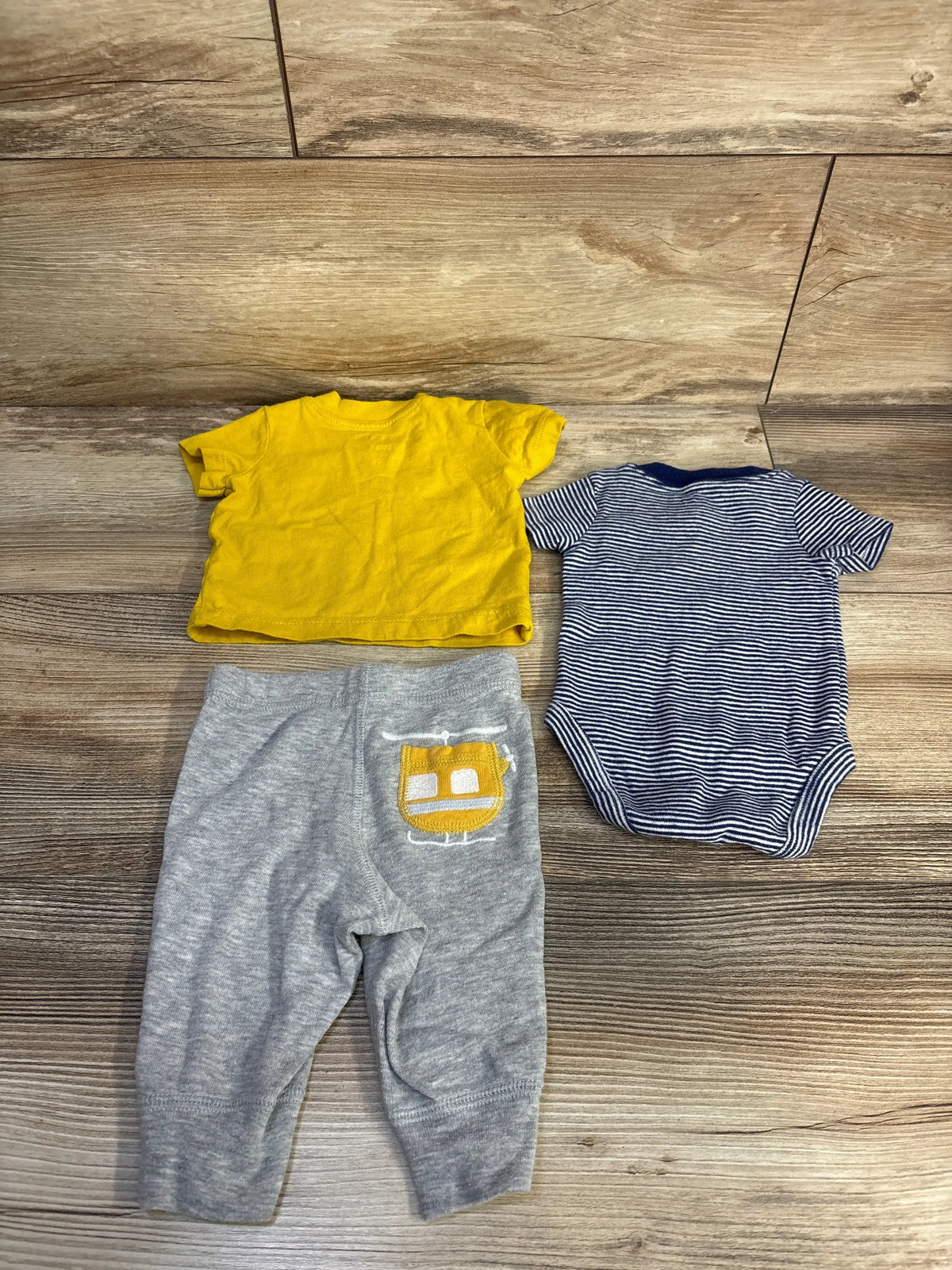 Flat lay of Carter’s newborn shirt, bodysuit, and pants set in yellow, navy stripes, and gray on wood-look floor