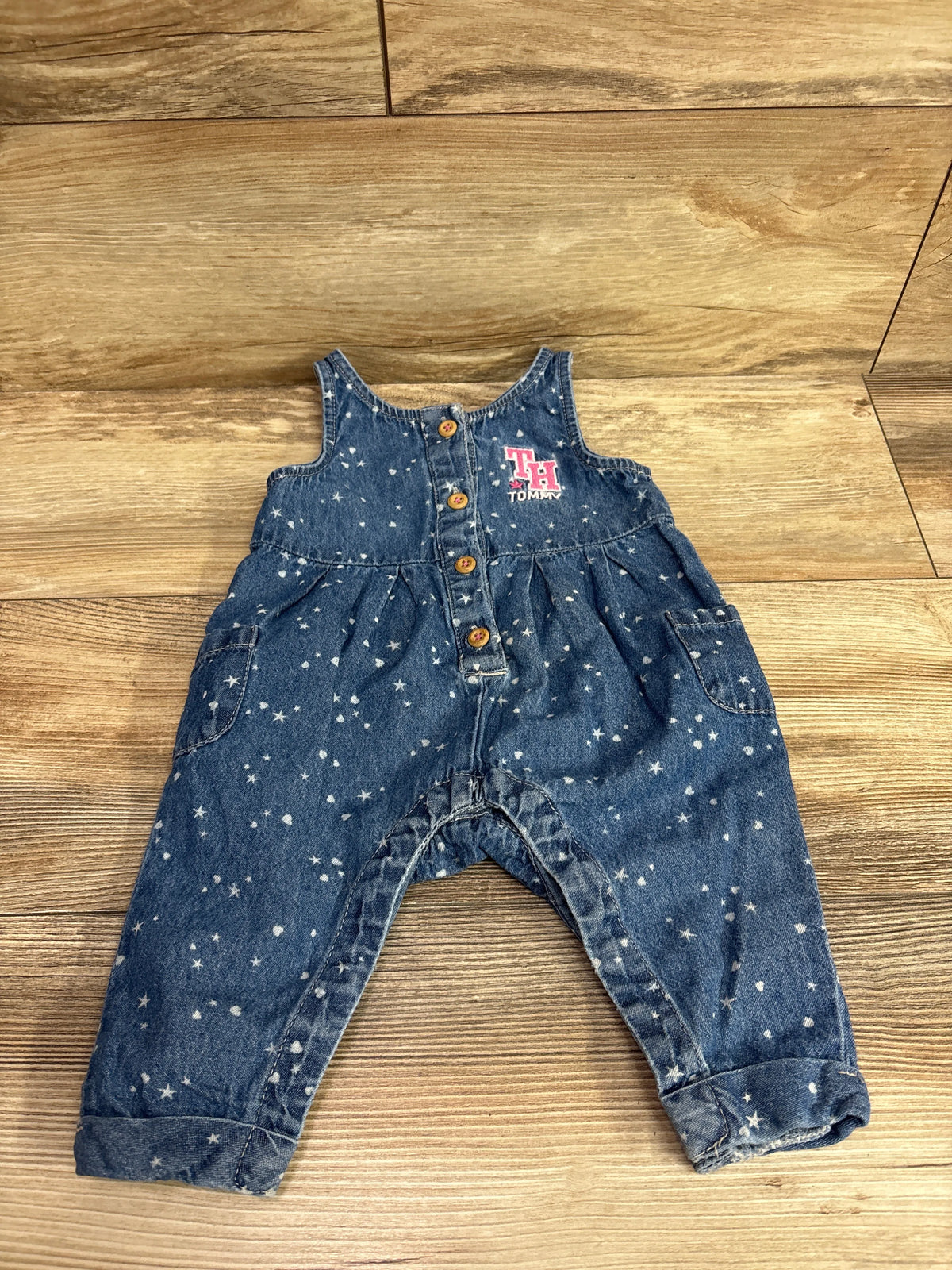 Front view of blue chambray sleeveless jumpsuit showcasing star print, button front, pockets, and Tommy logo on wood floor
