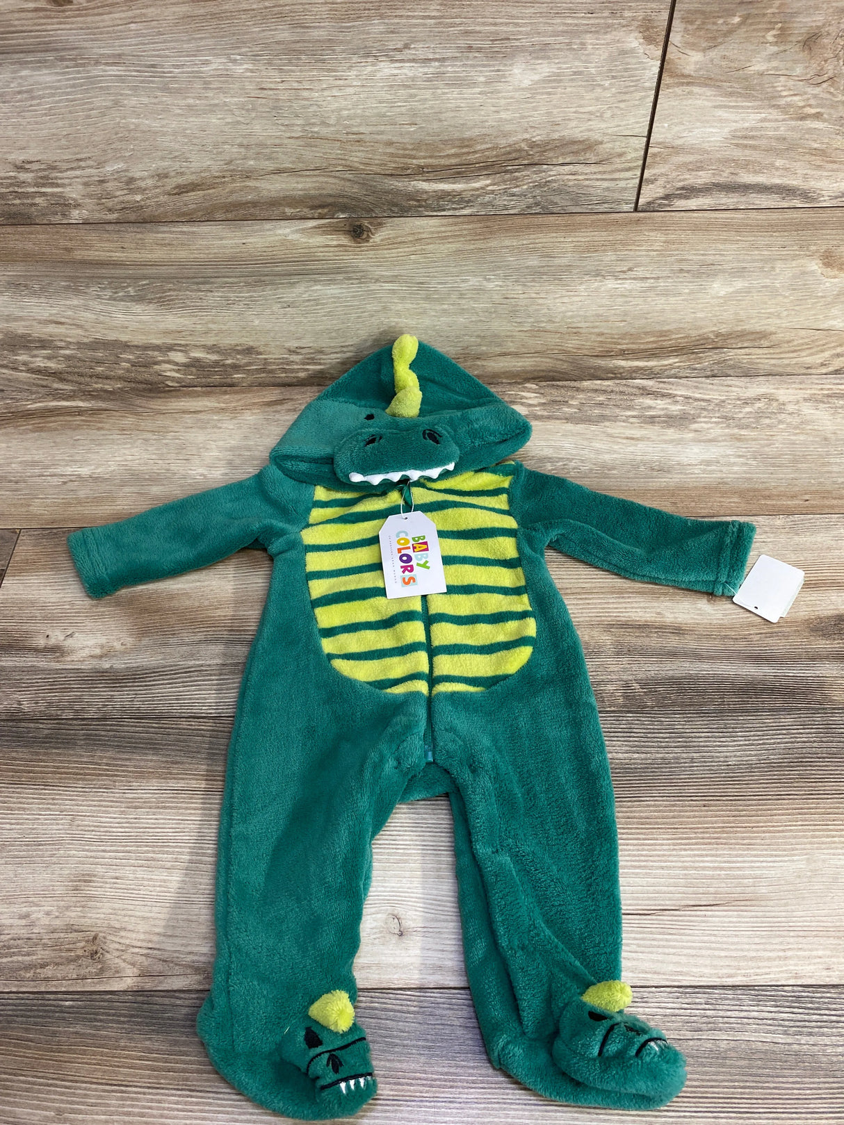 Green and yellow striped baby dinosaur costume onesie with hood and foot covers on wooden floor