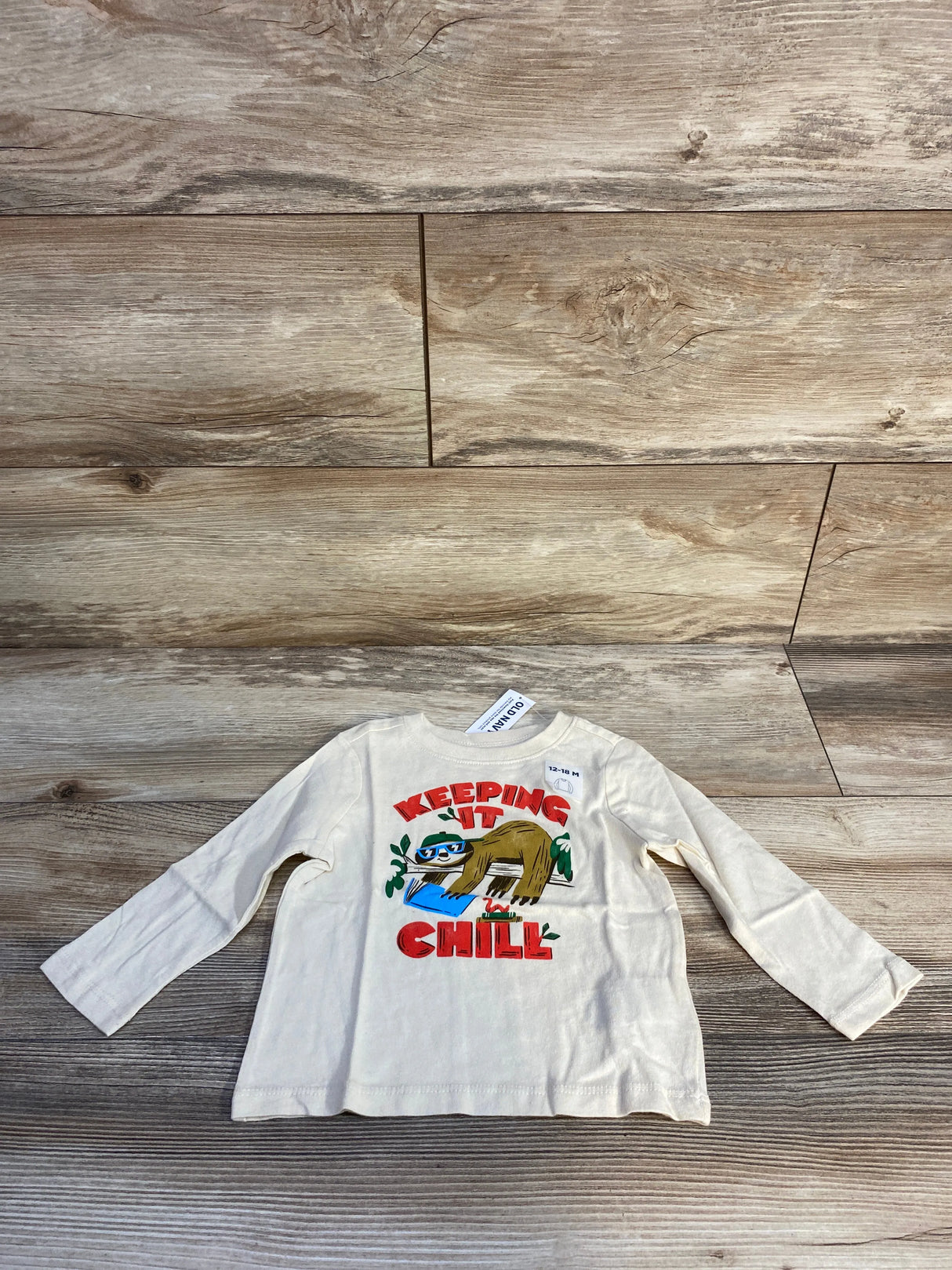 Cream toddler shirt with sloth graphic and 'Keeping It Chill' text on wooden floor