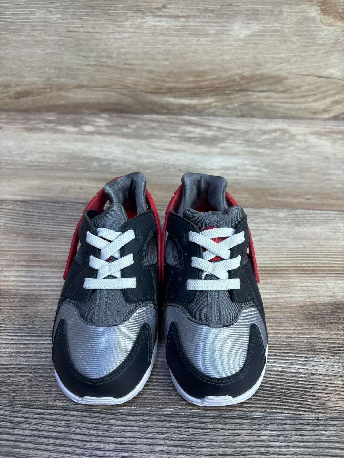 Front view of Nike Huarache Run TD toddler sneakers in grey and red with white laces on wood background, size 8C